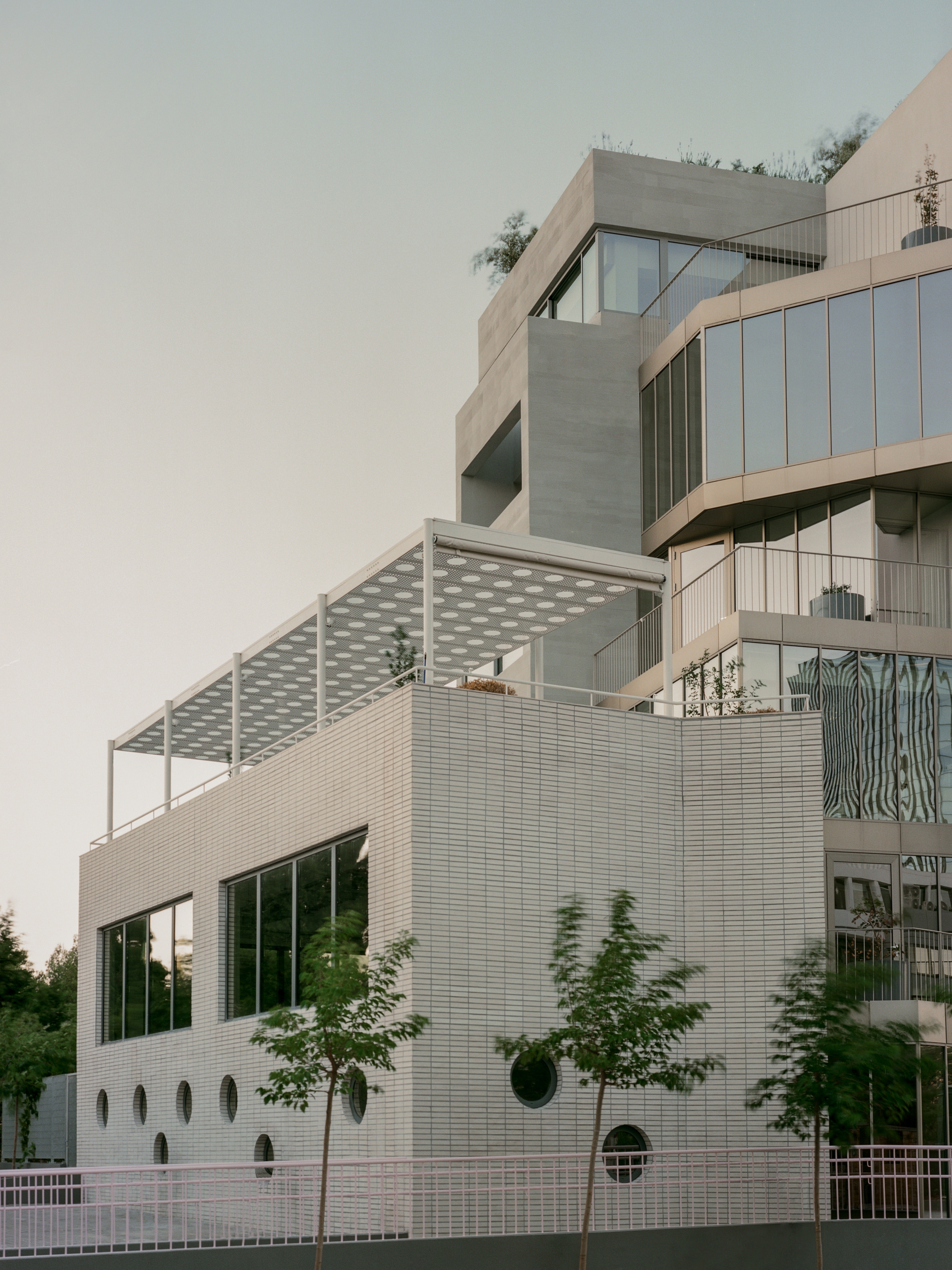 Stacked balconies with white tile cladding and circular openings beneath a perforated canopy at dusk