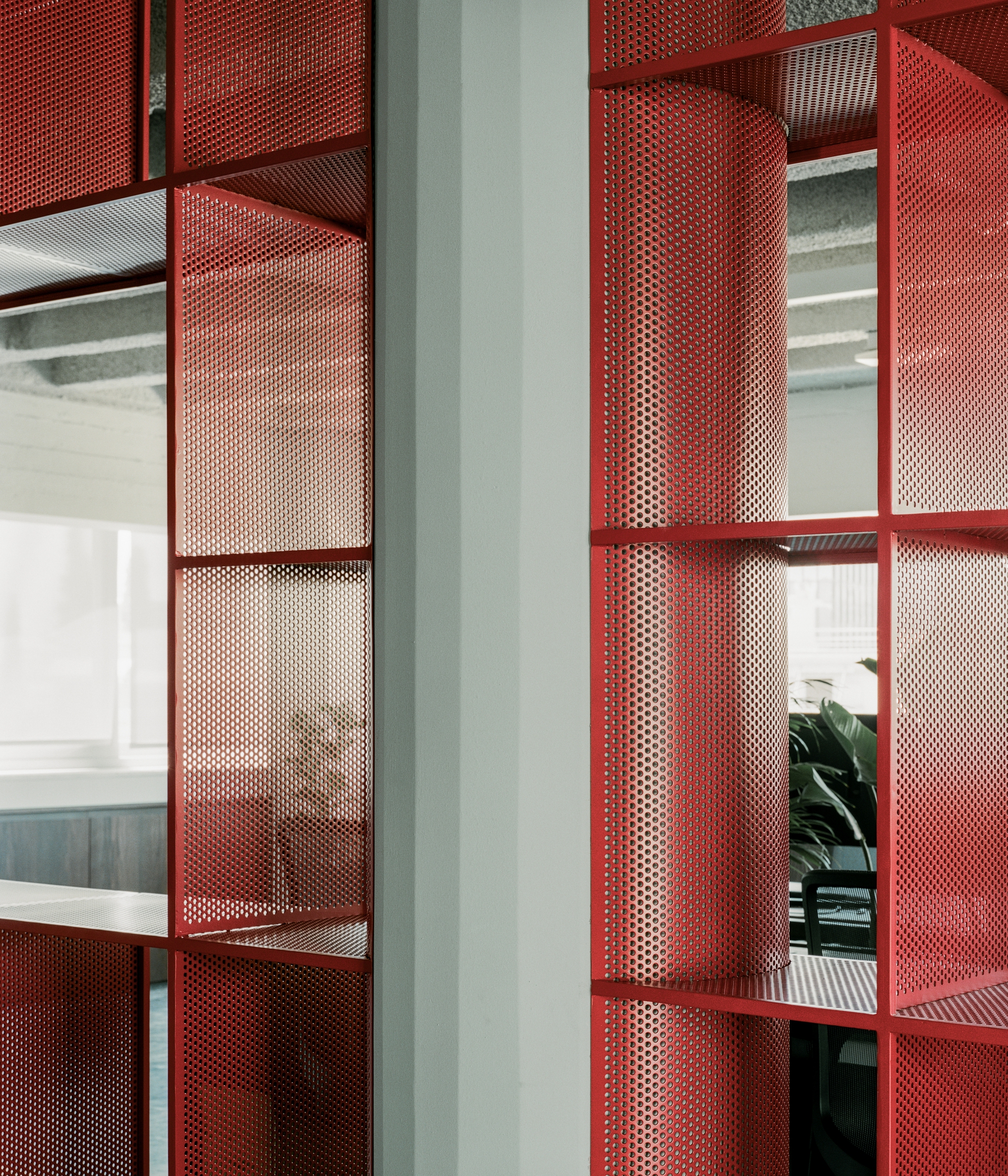 Close-up of red perforated metal shelving units with curved segments reflecting light from workspace beyond