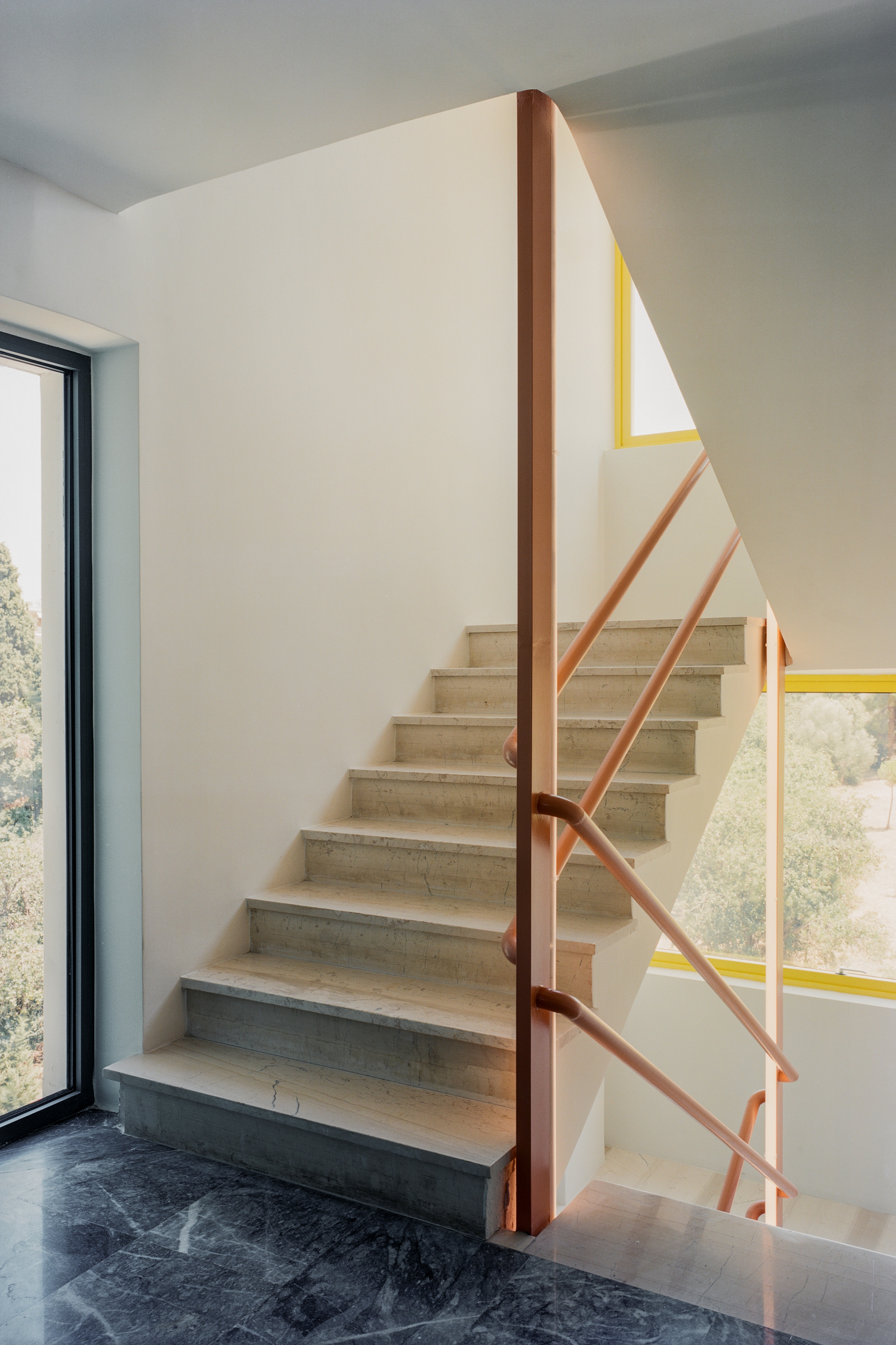 Internal staircase with light stone treads and terracotta metal railing with geometric yellow accent bands