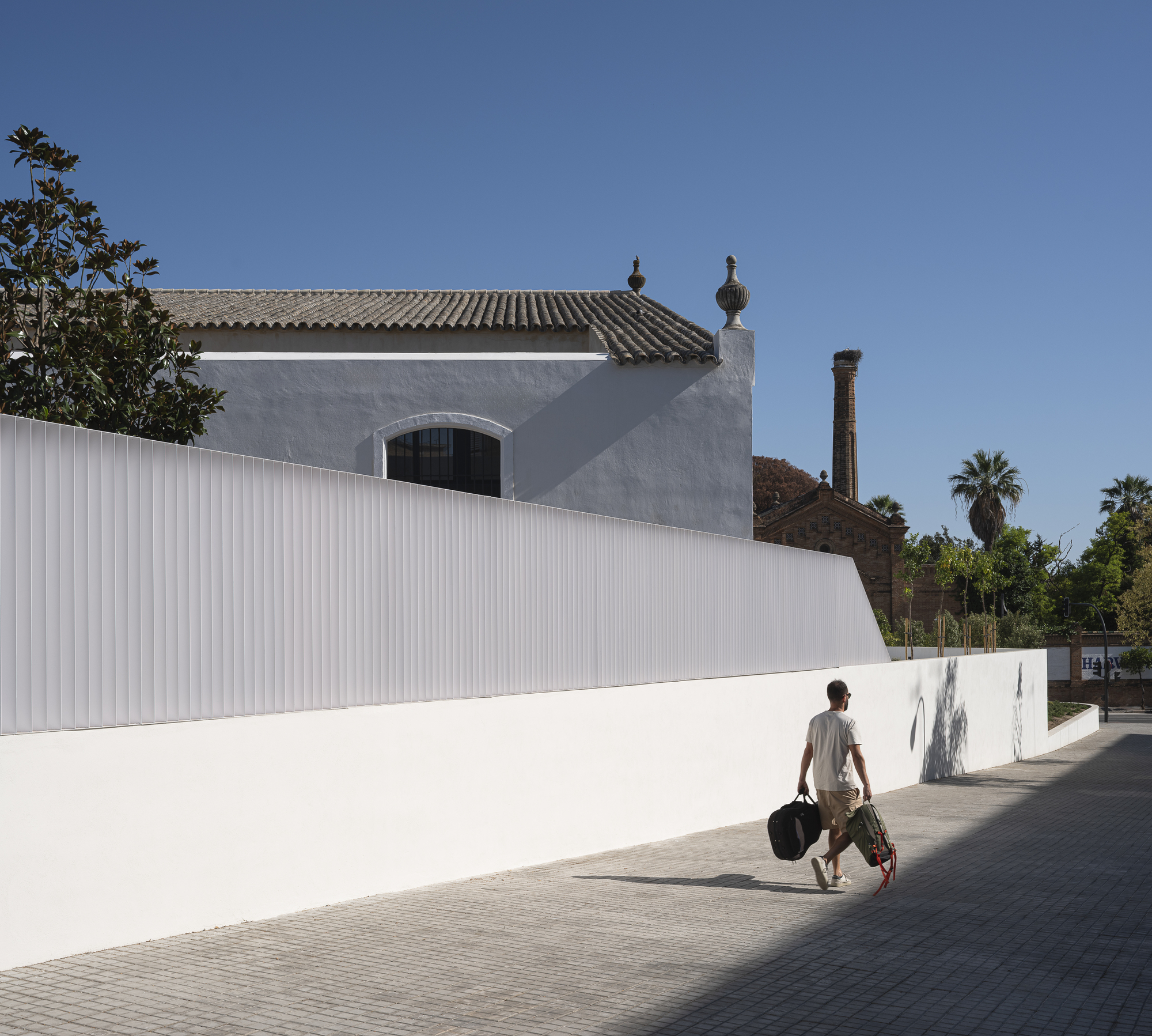 Pedestrian sidewalk and the white perimeter wall along the bodega's edge