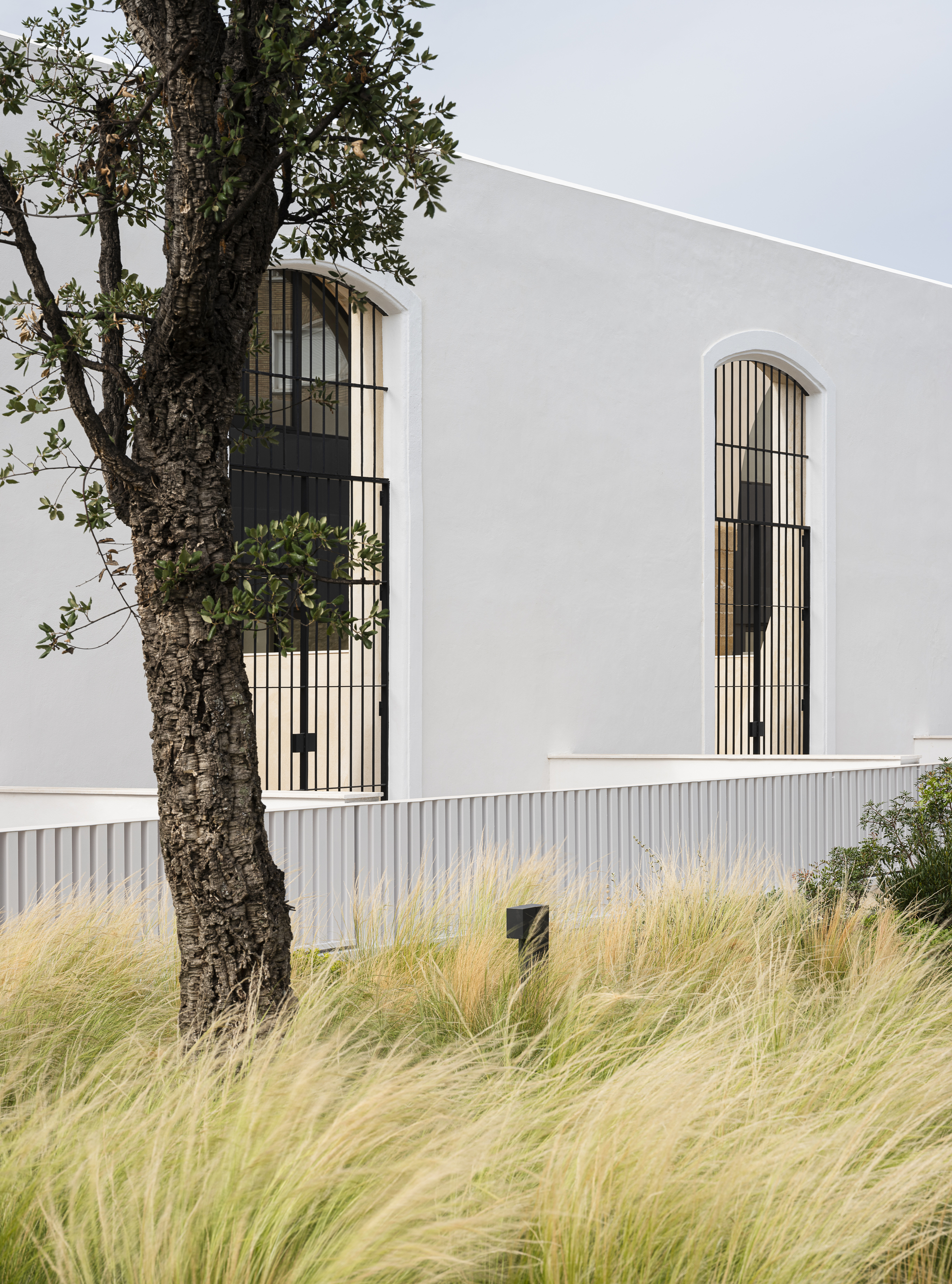Arched timber-screen window in the white facade with stipa grasses in the foreground
