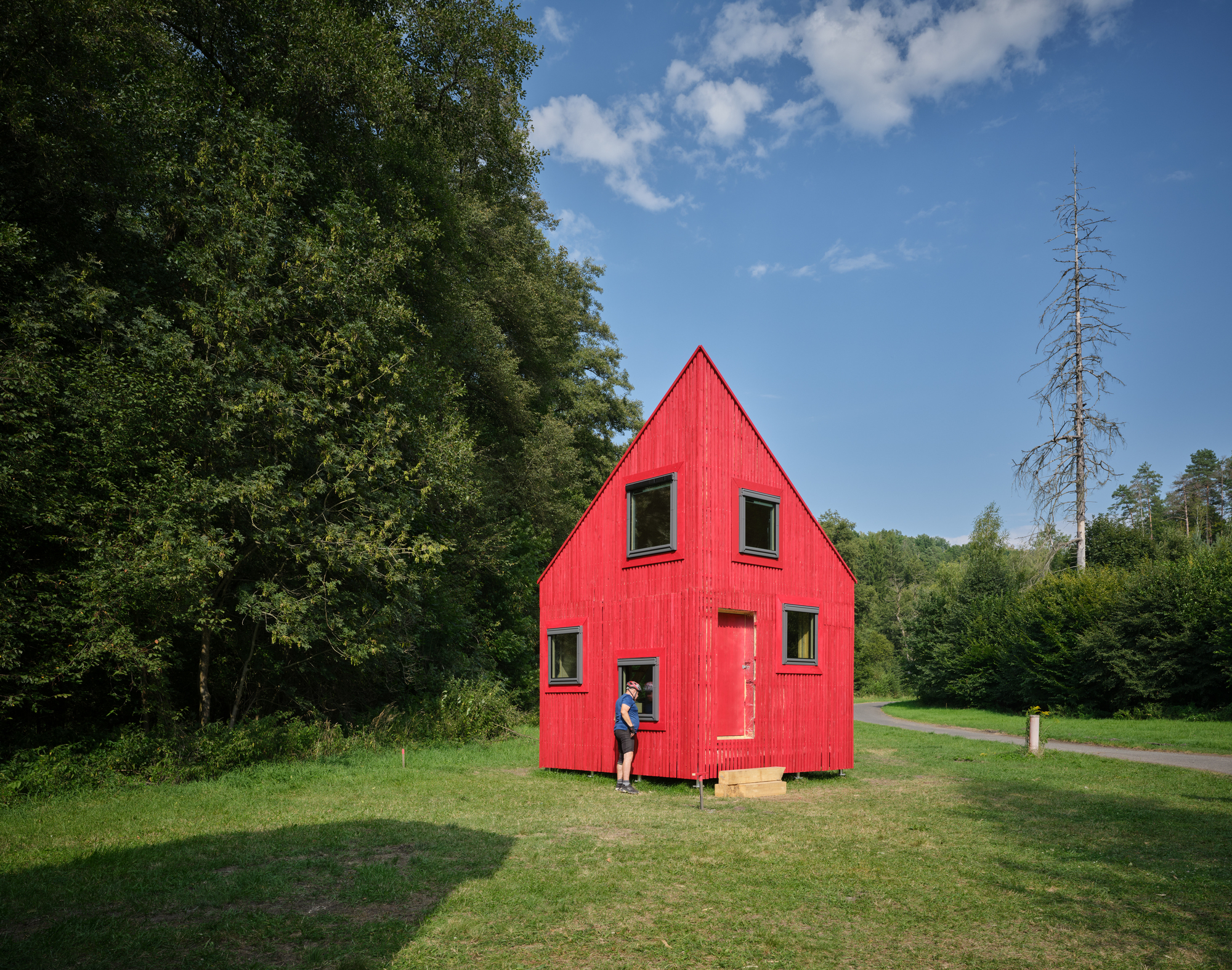 Red clad dwelling with peaked roof and a visitor standing in the doorway on a sunny day