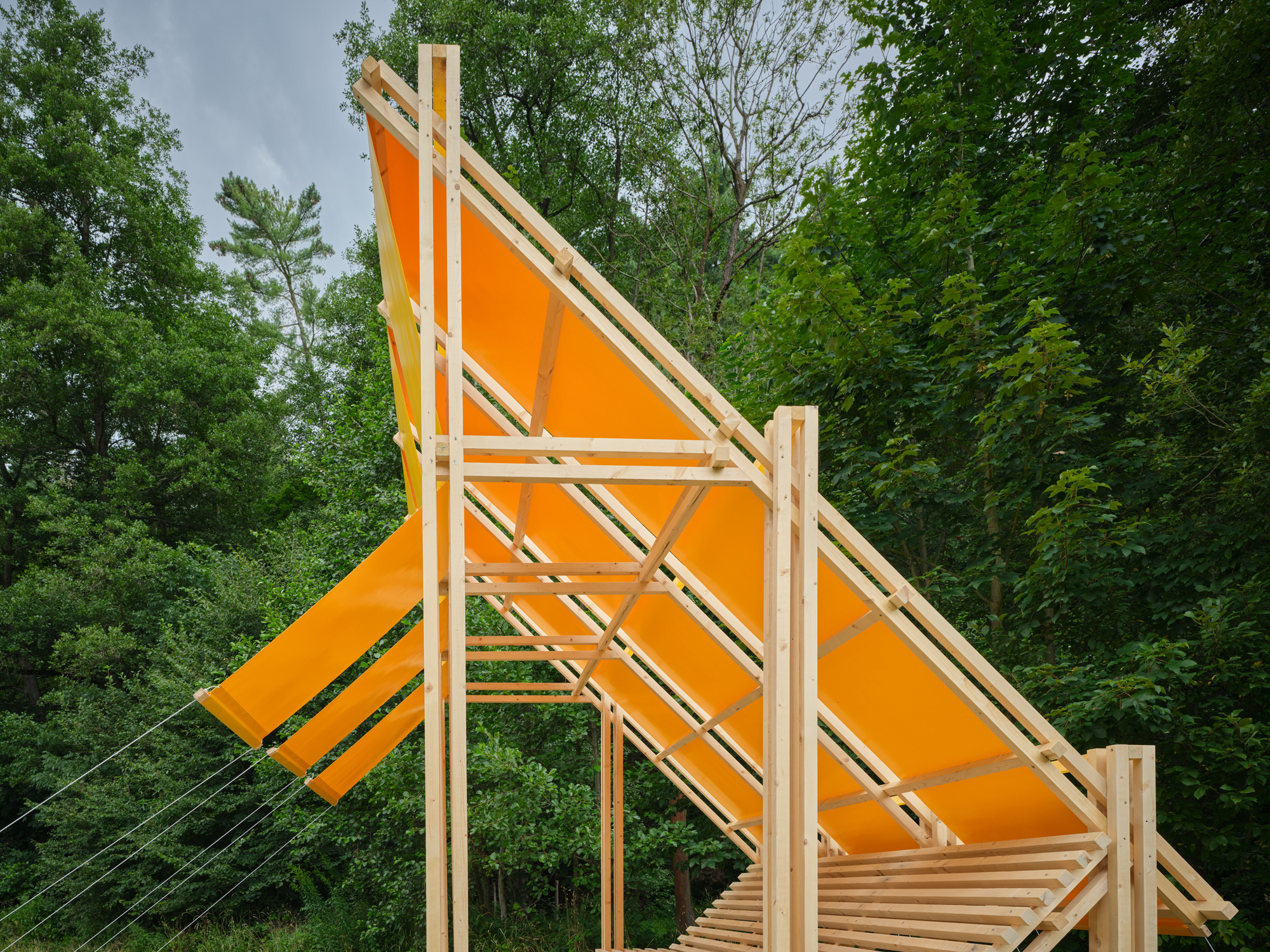 Orange fabric panels stretched across diagonal timber framing under cloudy skies