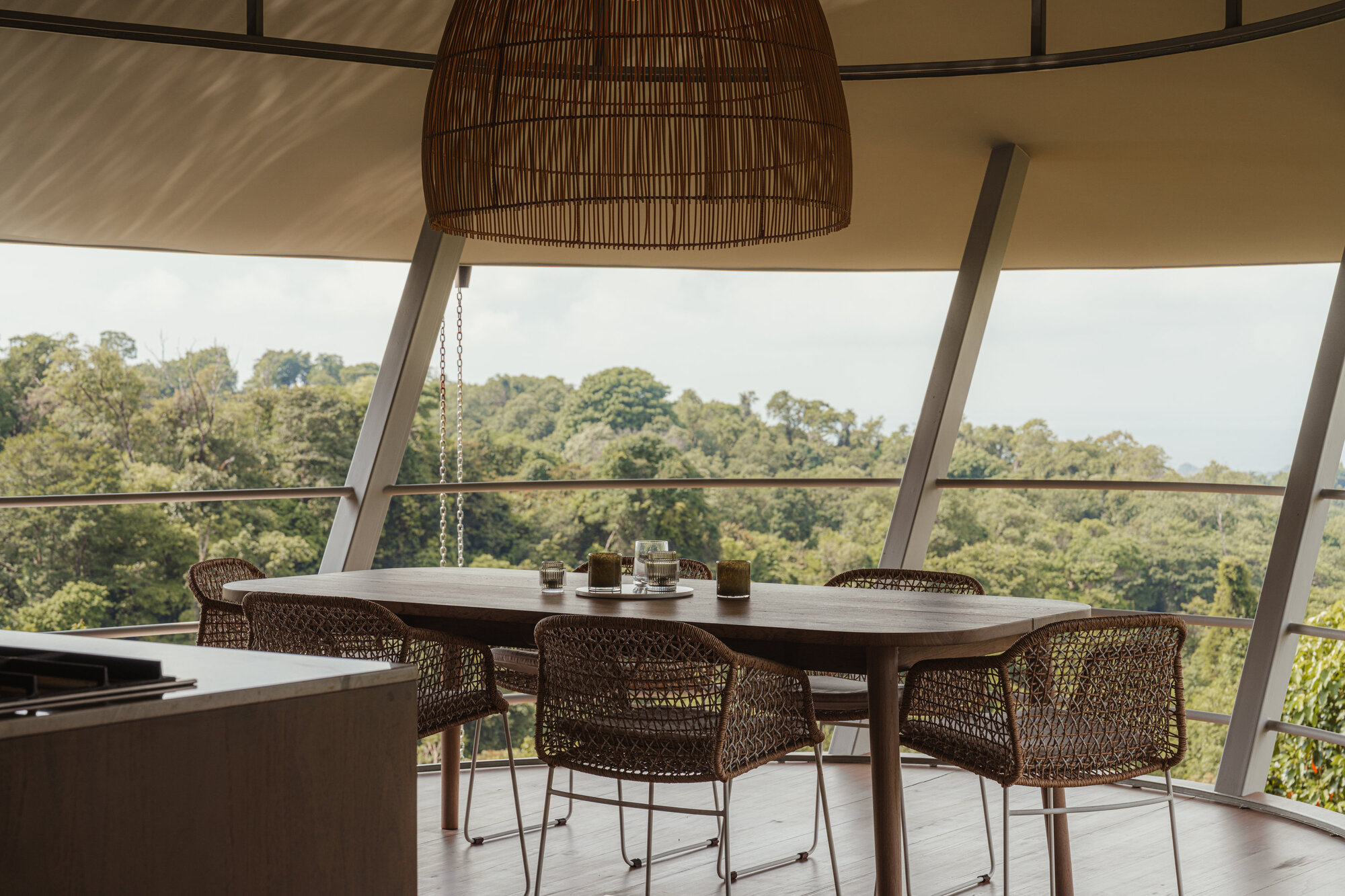 Kitchen and dining area with a long timber table and cane chairs framed by the curved glass wall