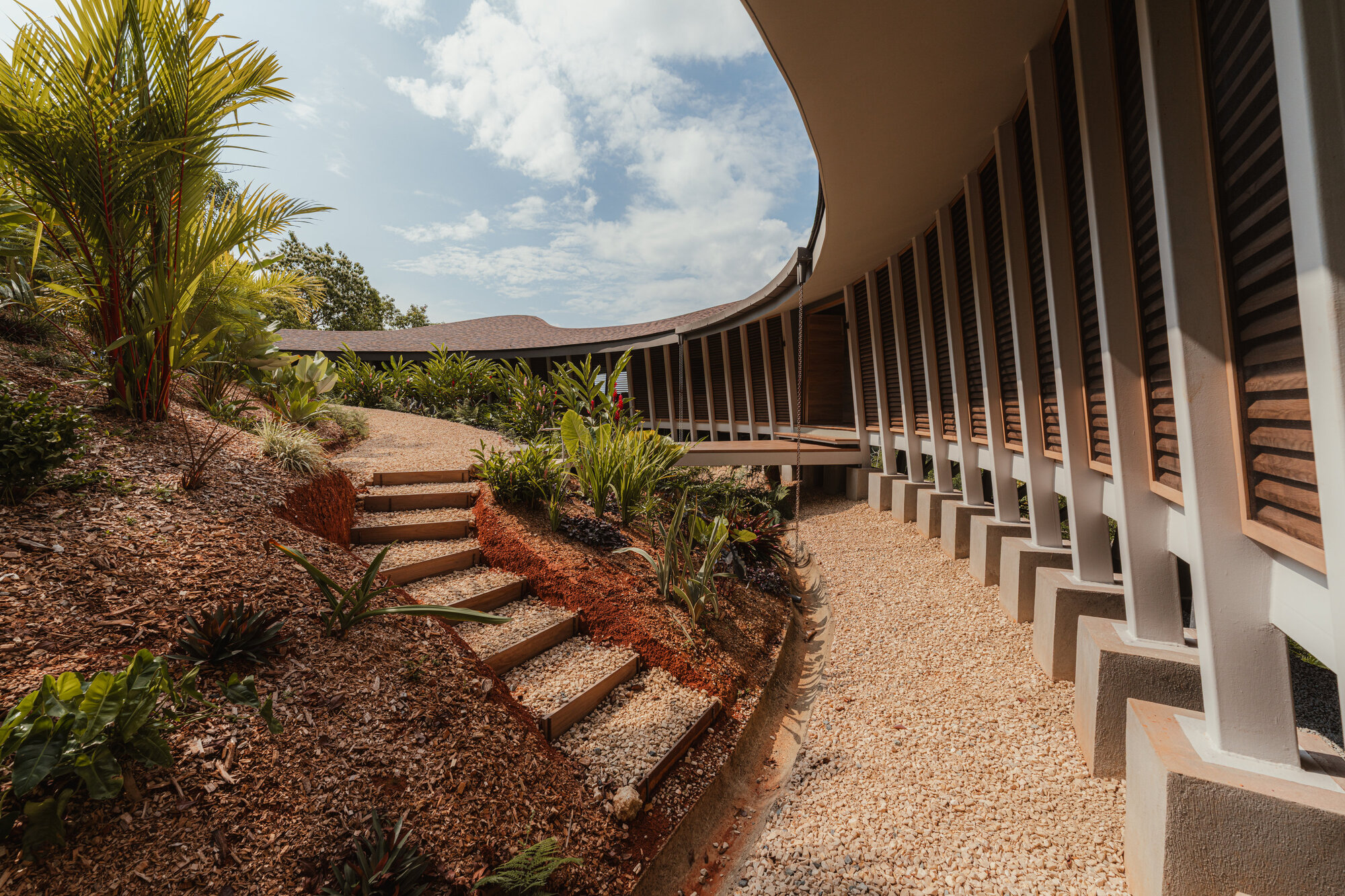 Exterior walkway with a gravel path along the side of the house beneath the overhanging curved roof