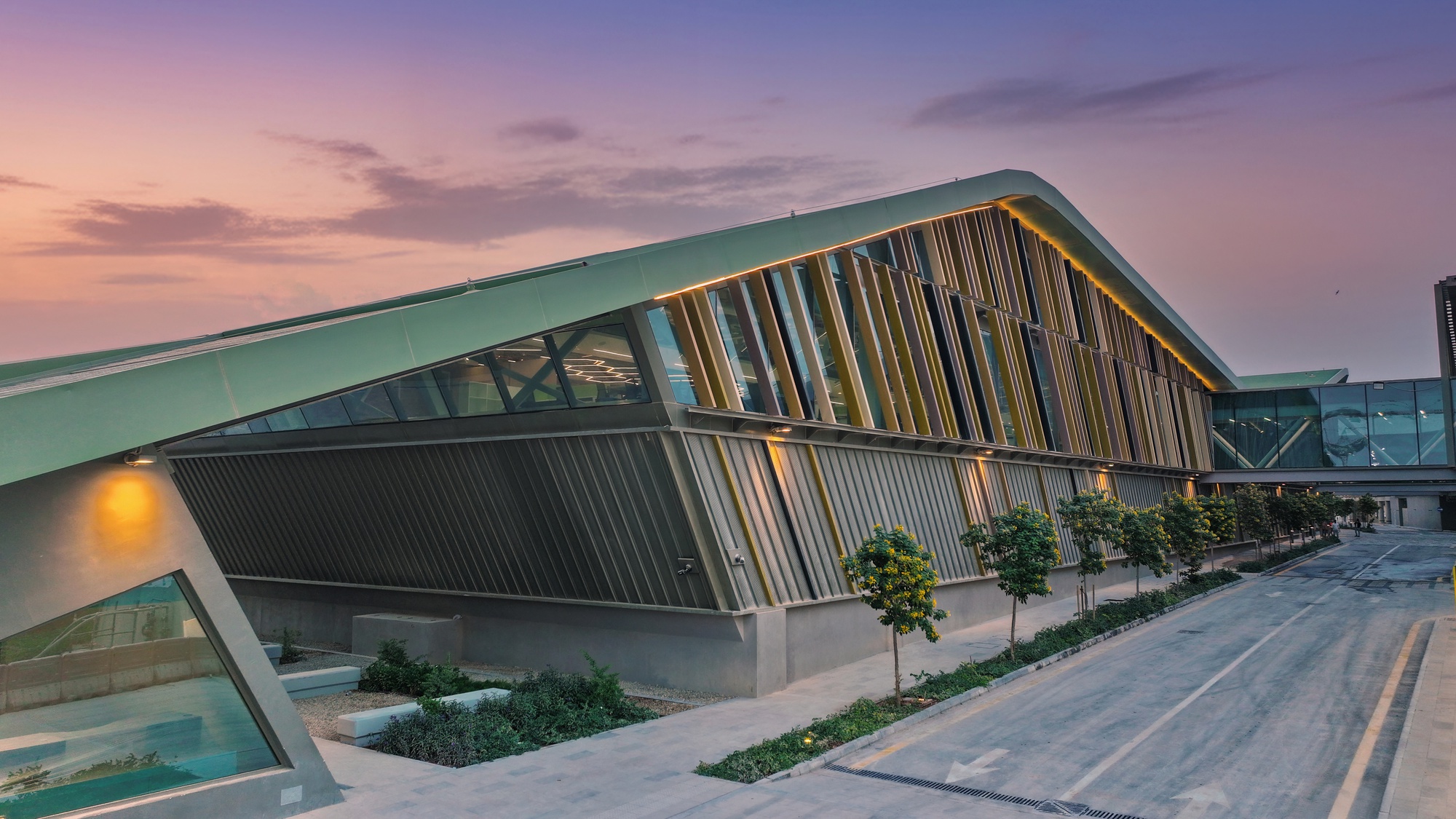Green metal roof edge with vertical timber louvers and planted beds at sunset