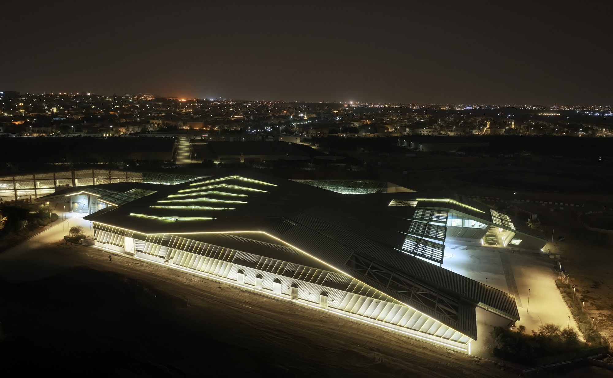 Aerial view of the terraced green roof and illuminated facades against the distant cityscape at night