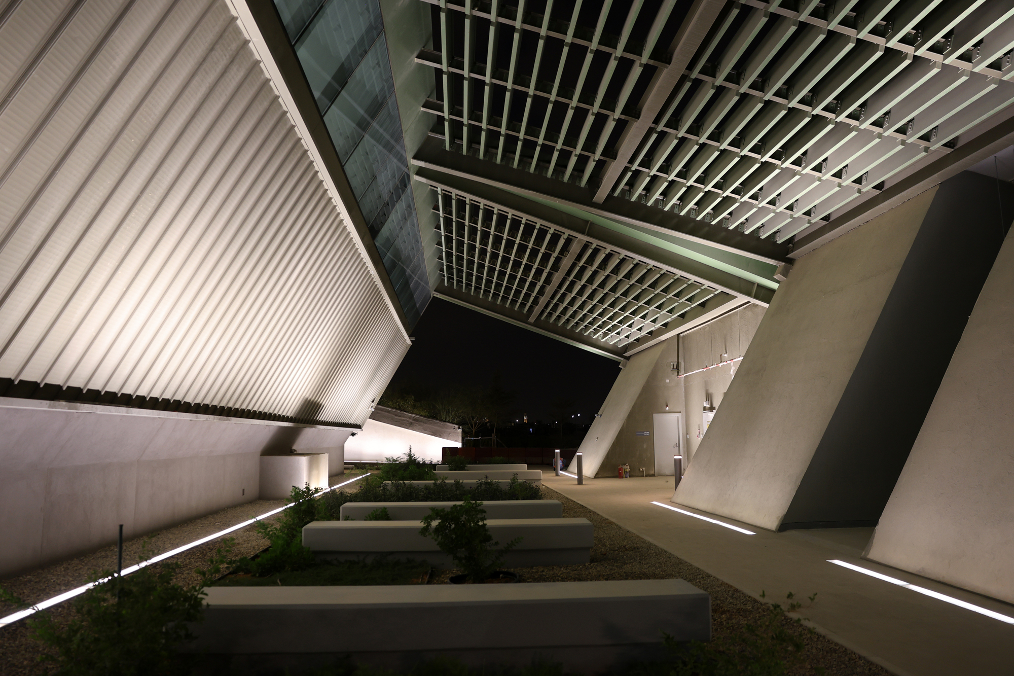 Exterior courtyard with raised planted beds beneath the cantilevered ribbed ceiling and angular walls at night