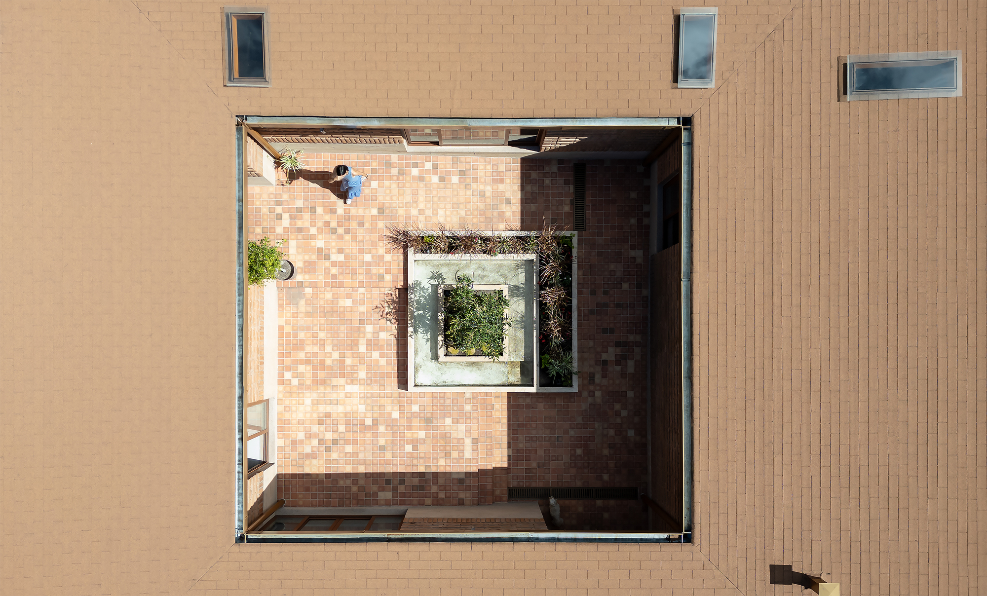 Overhead view of an internal courtyard with checkered brick paving and a central planted bed