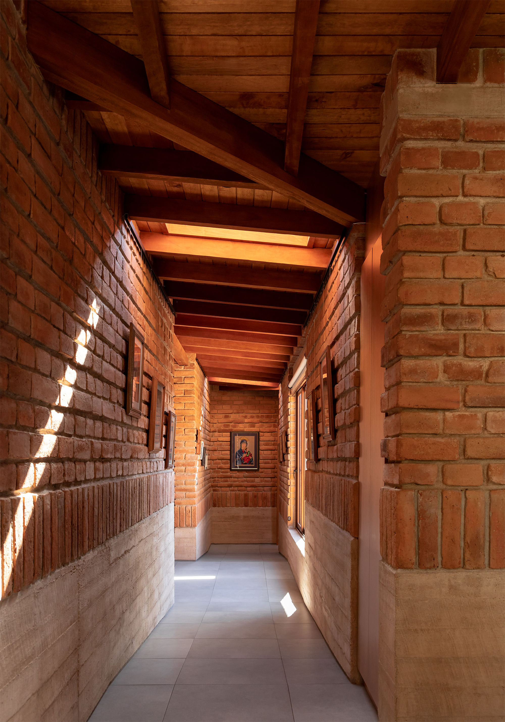 Narrow corridor with exposed brick walls, timber ceiling beams and skylights casting diagonal shadows on the floor