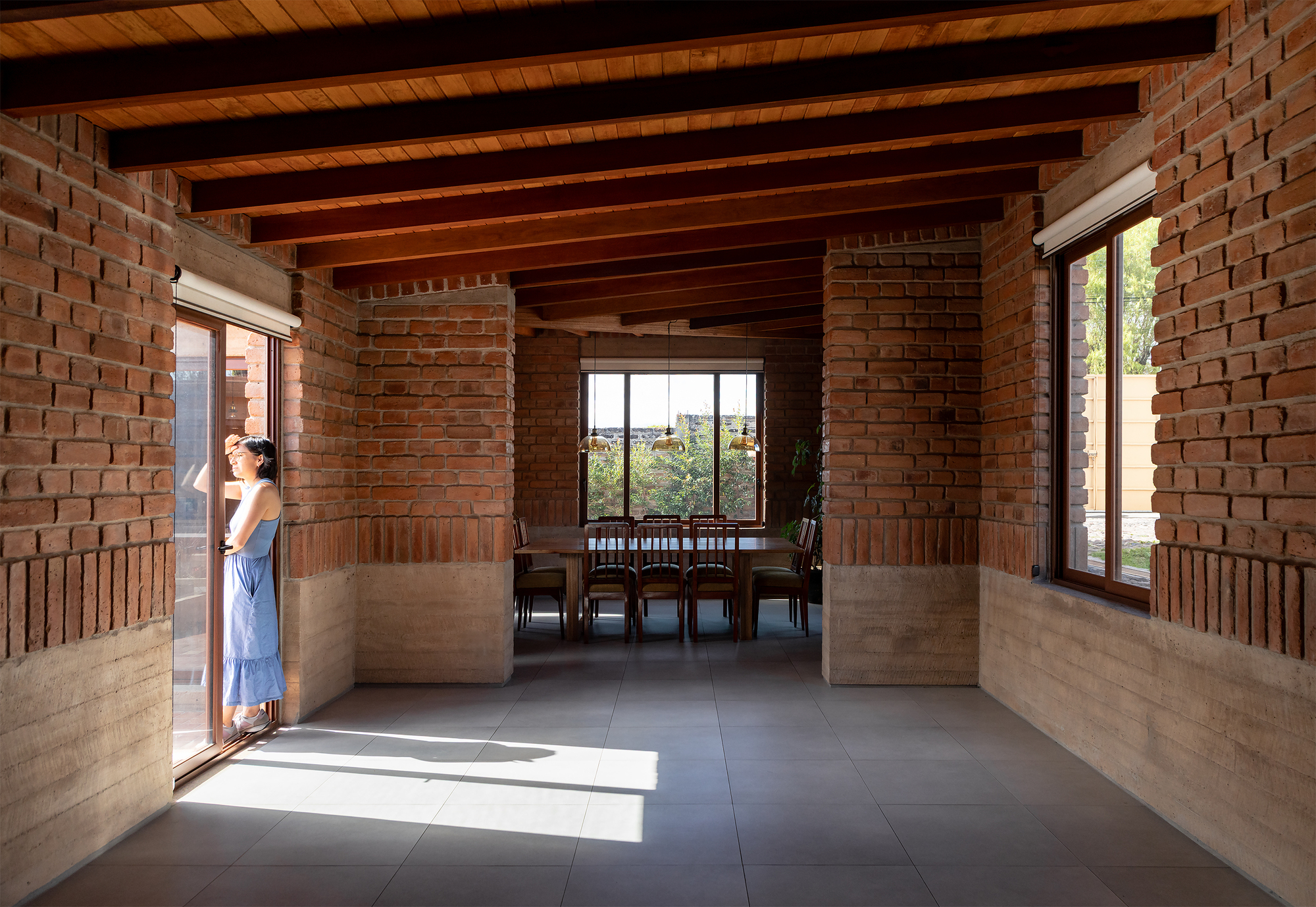 Open living space with brick walls, exposed timber beams and a figure standing in doorway light
