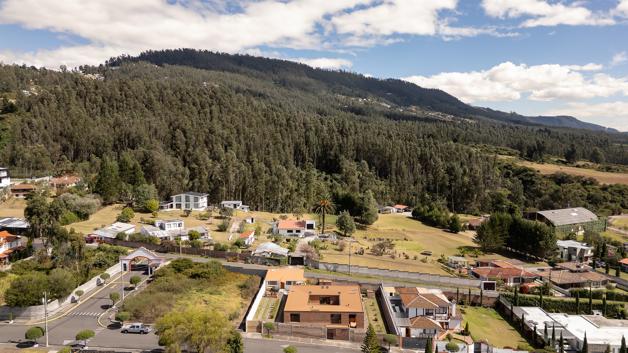 Aerial view of the brick residence within a valley neighborhood below forested mountains
