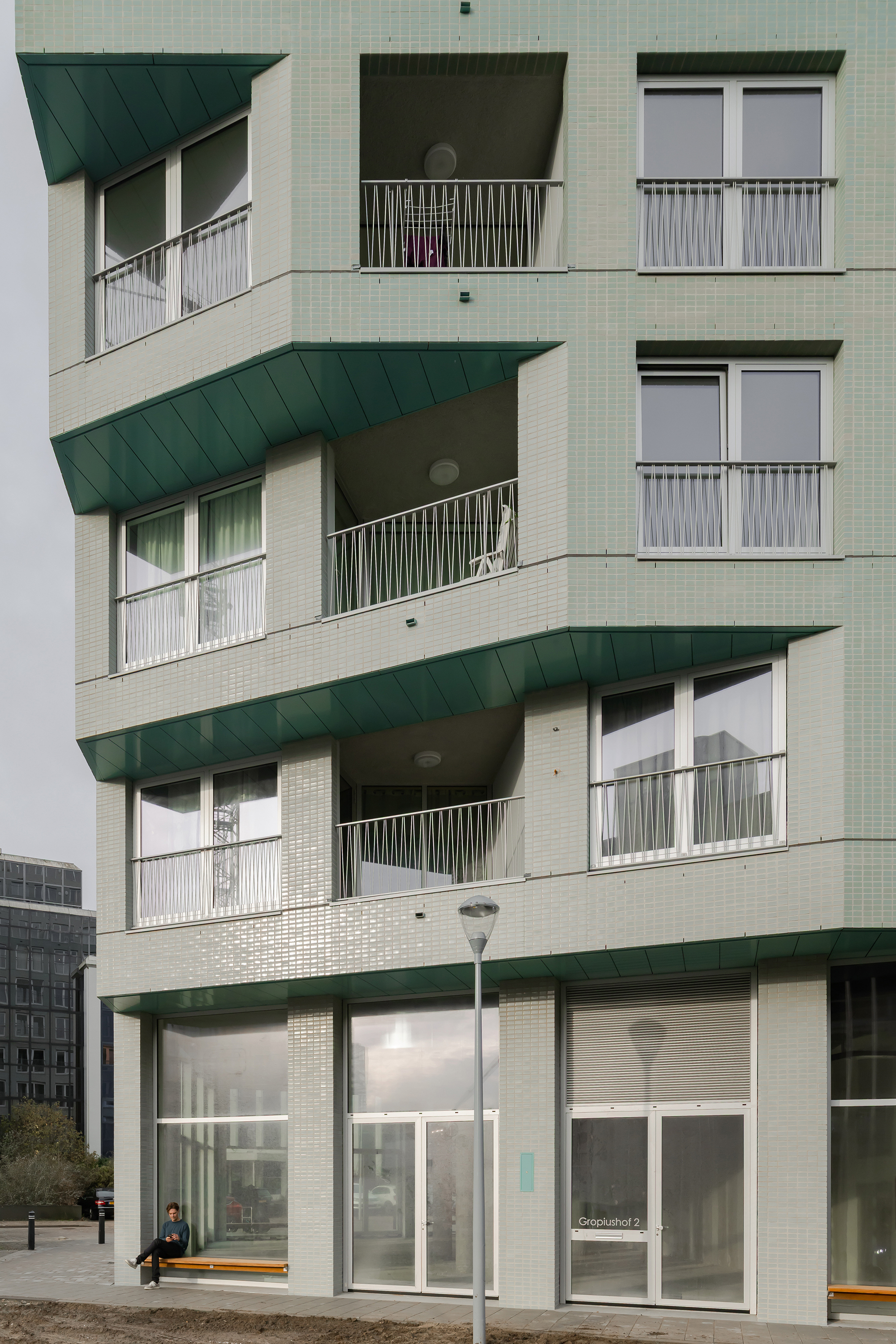 Stacked balconies with dark green canopies and metal railings above the ground-floor entrance on a cloudy afternoon