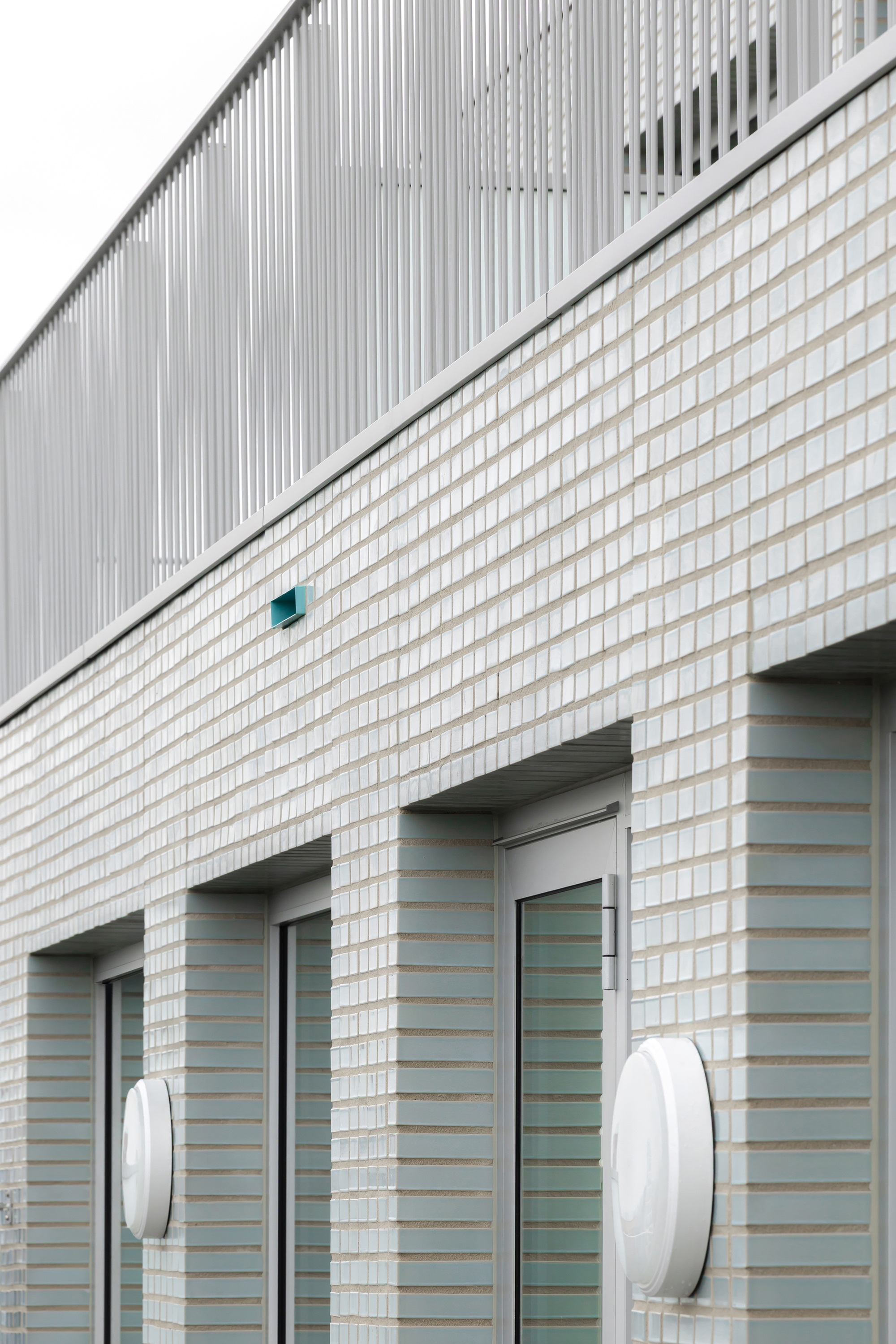White brick facade with diagonal division line, entrance openings and circular wall-mounted light fixtures