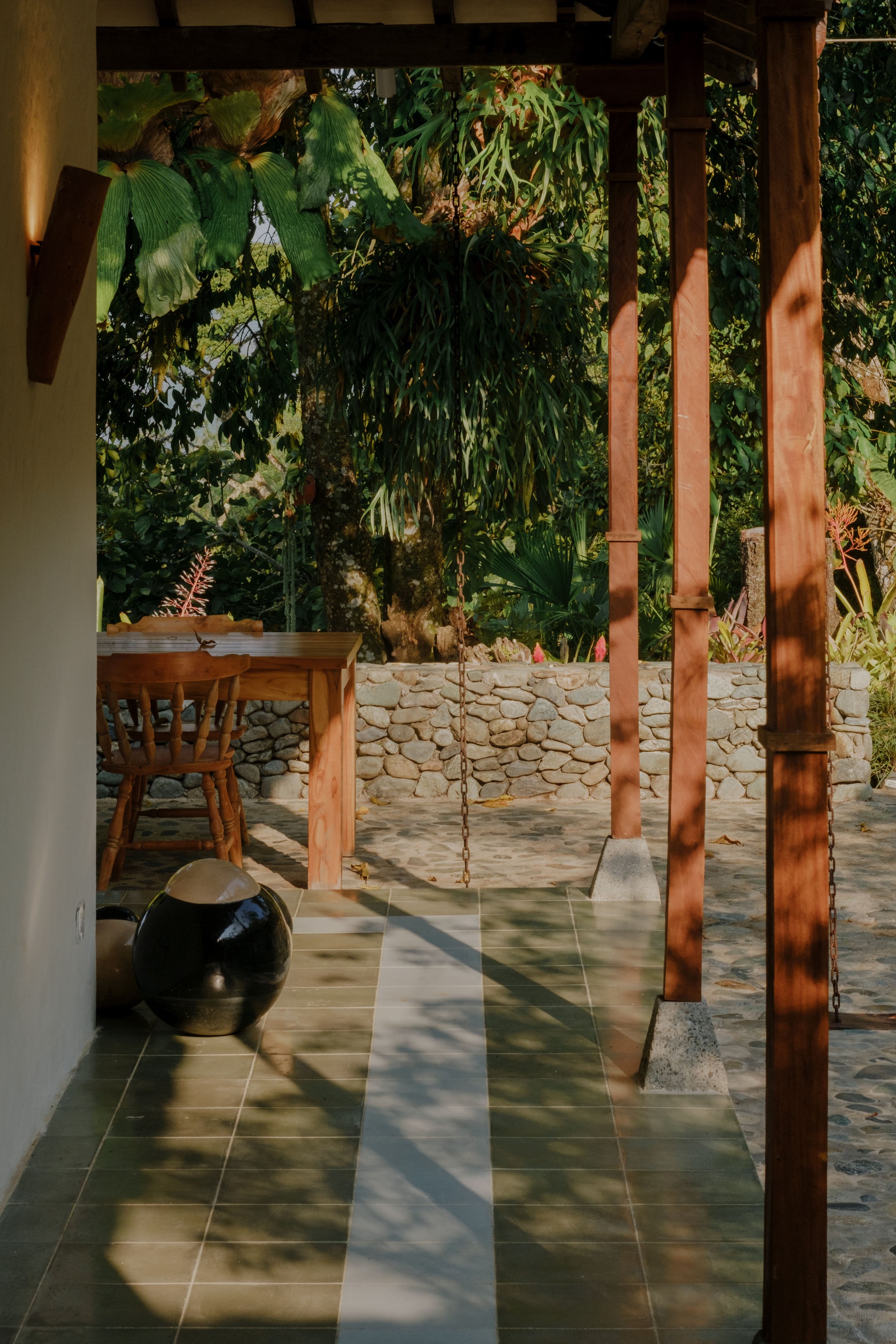 View through timber columns to stone retaining wall and garden in afternoon light