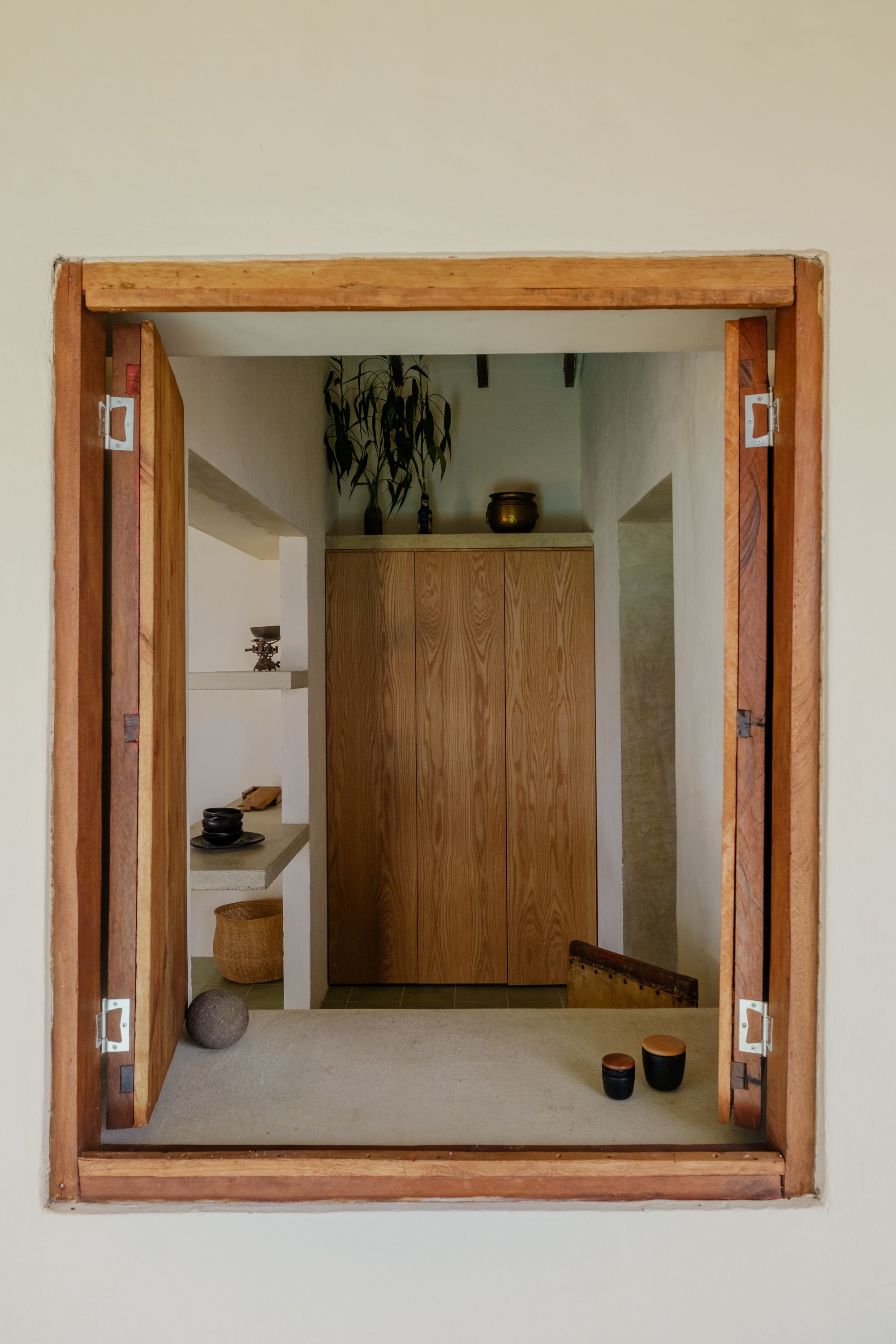 Timber-framed window opening onto interior foyer with wooden cabinet and display shelves