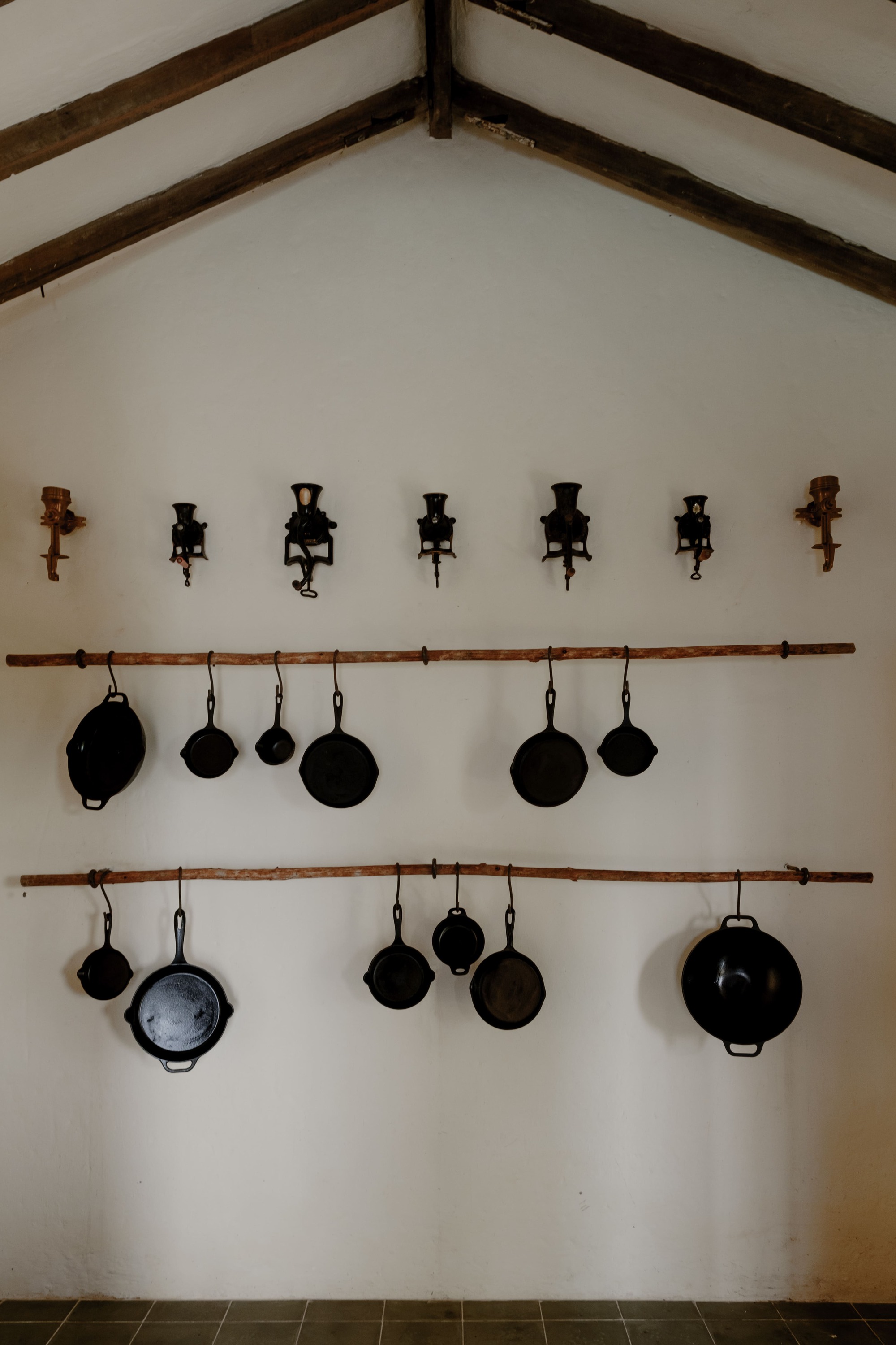 Vaulted interior wall with exposed timber beams, hanging cast iron pans and wall-mounted candle sconces