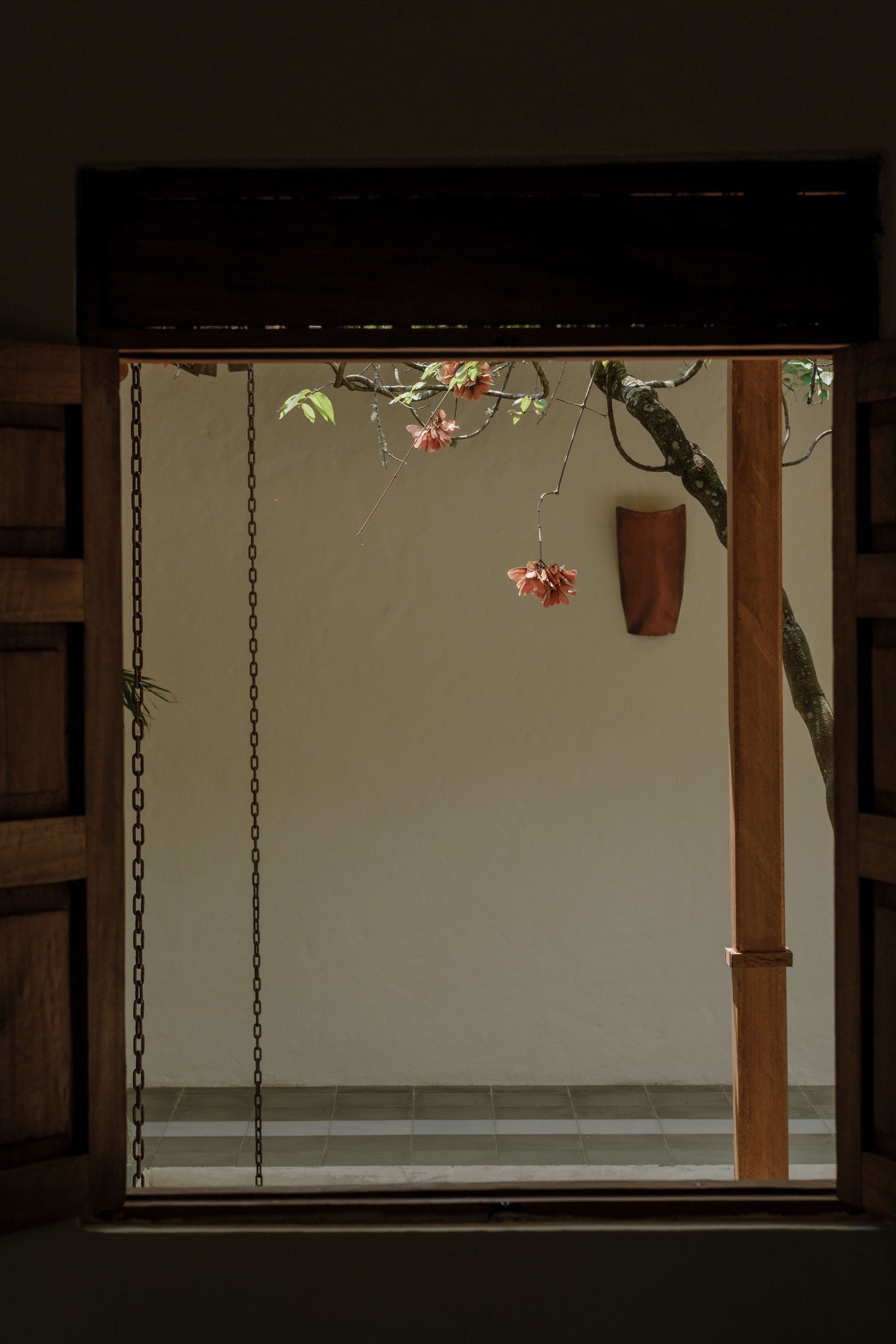 Window framing a view of a wooden column and flowering tree branch against a pale exterior wall