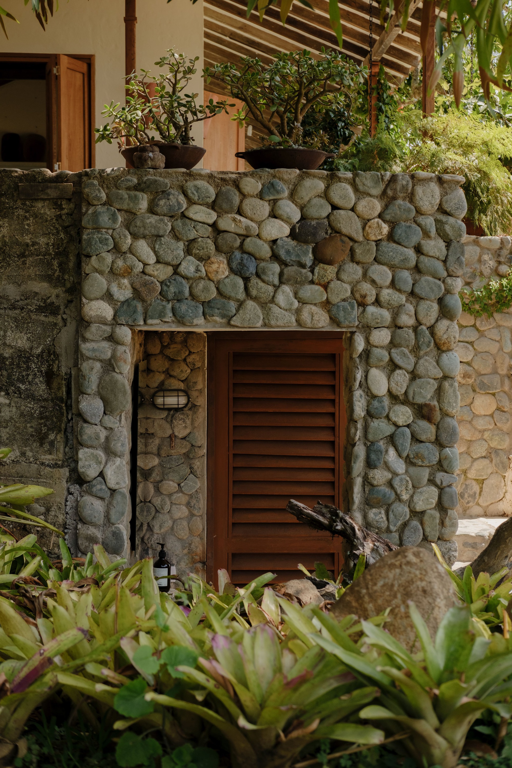 River stone wall surrounding a louvered timber door with planted bed of succulents and shrubs