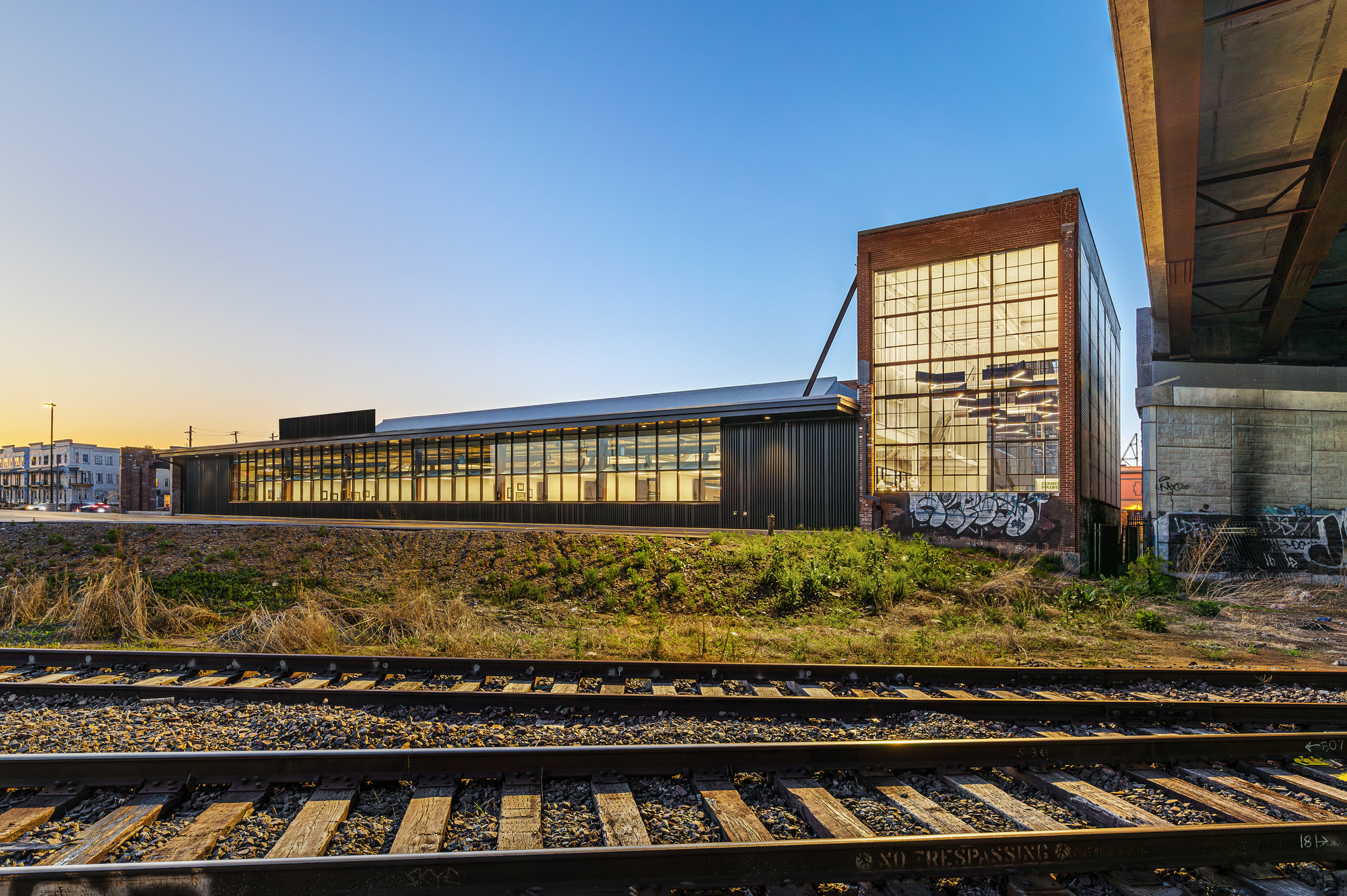 Glass-fronted facade with tower element viewed across railroad tracks at dusk