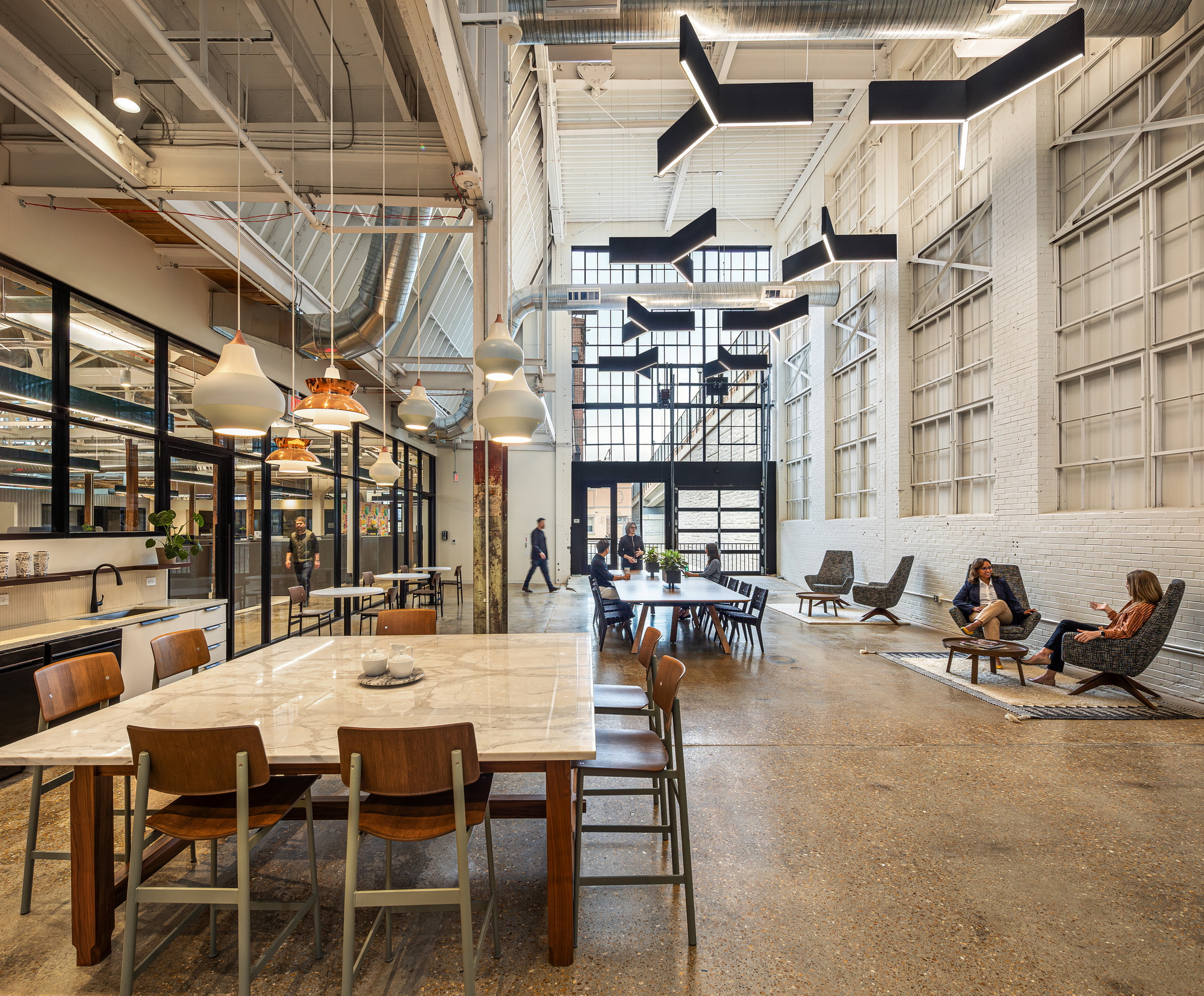 Double-height workspace with painted white brick walls, suspended black sculptural forms and timber ceiling