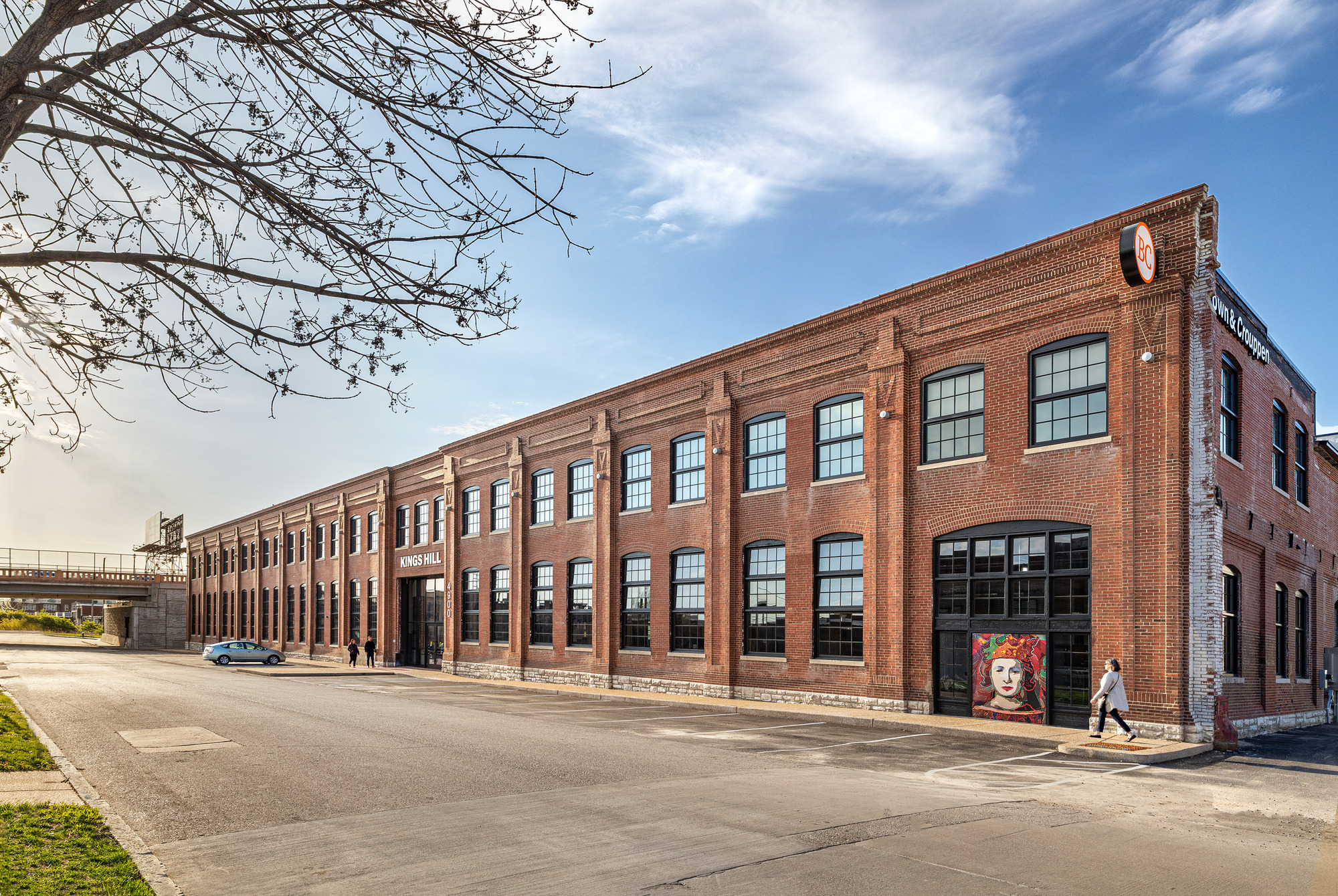 Streetview of the red brick warehouse facade with large industrial windows and pedestrians passing