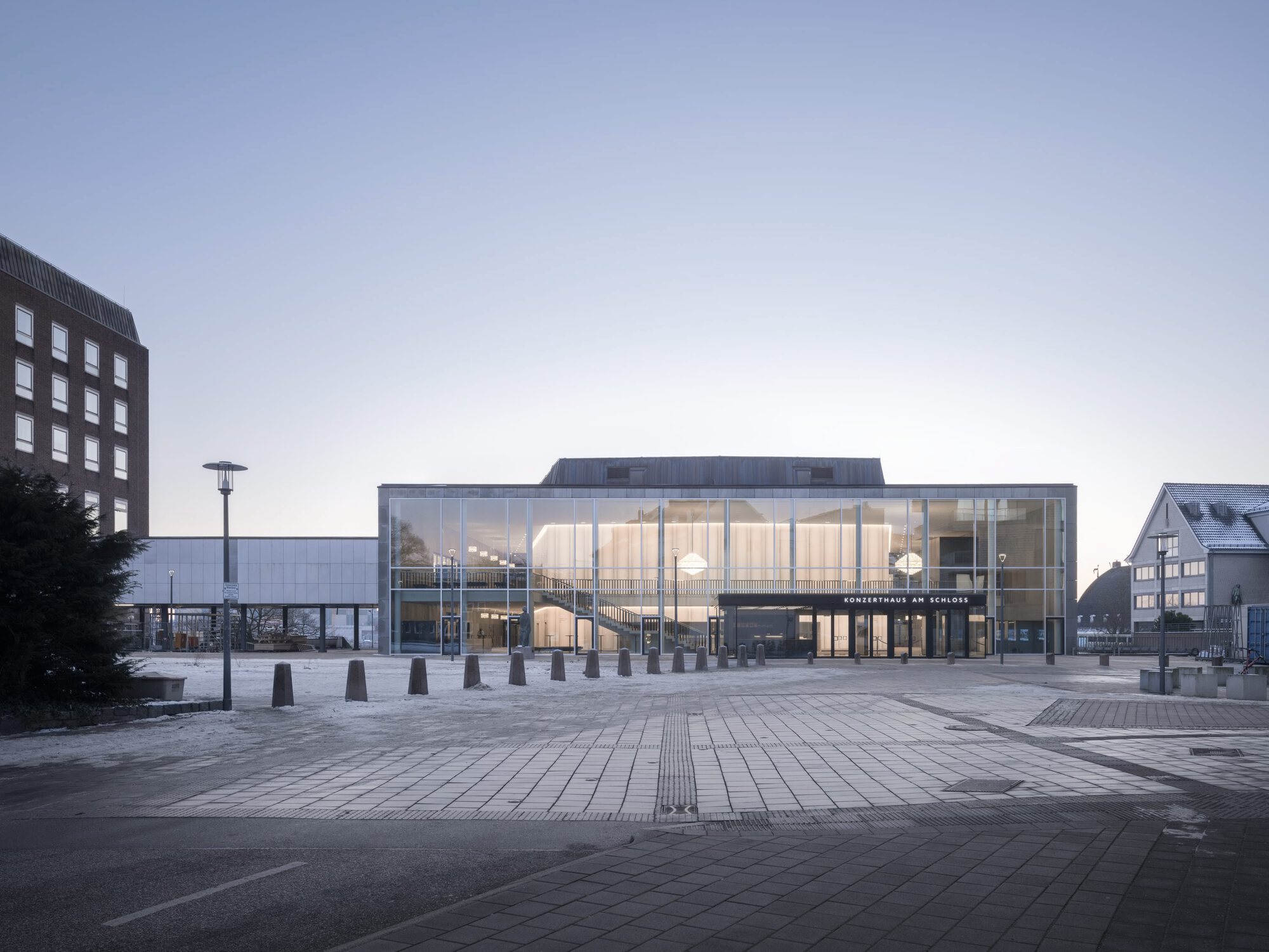 Glazed facade of the concert hall overlooking a paved plaza at dusk
