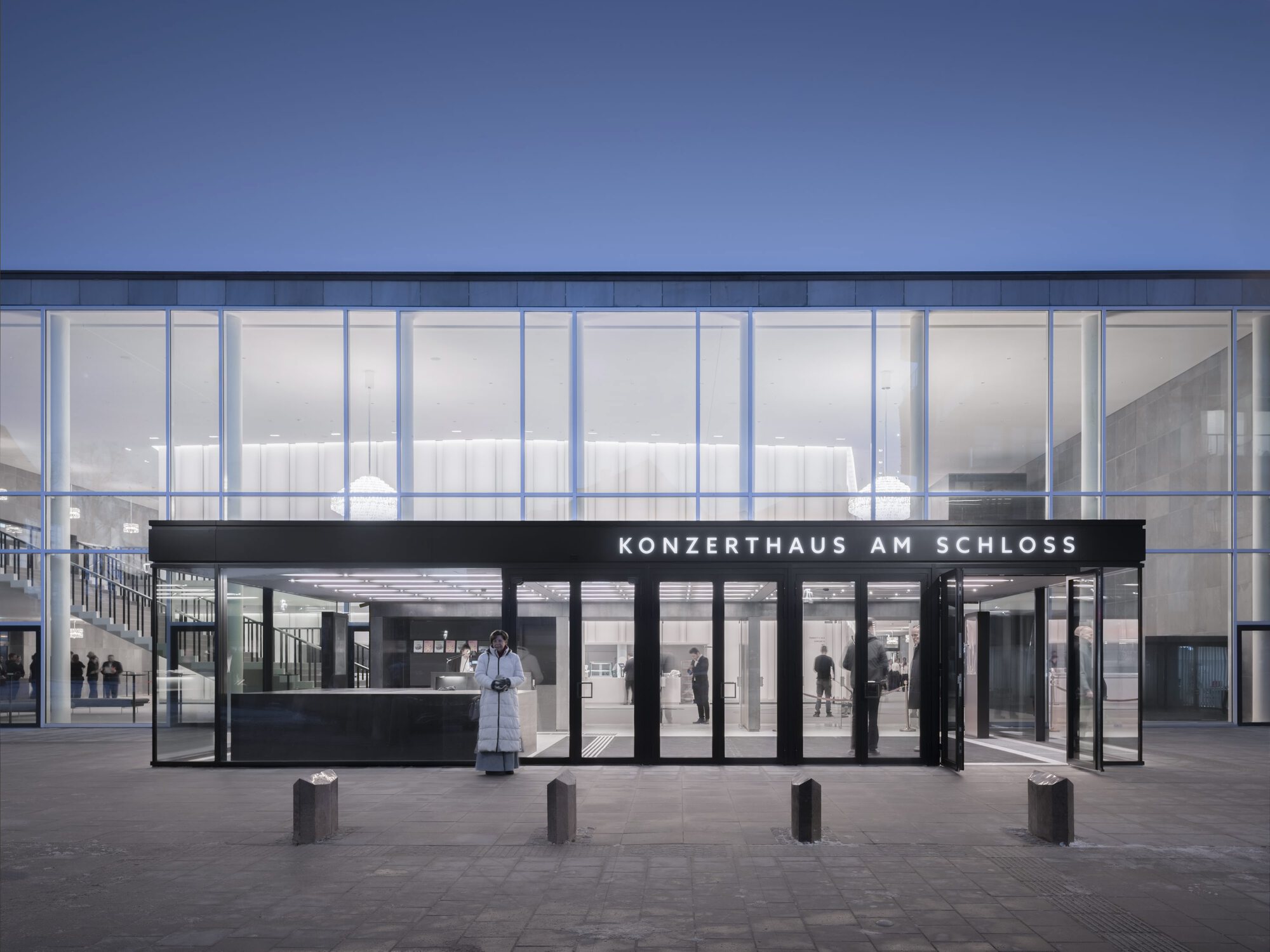 Ground-level entrance canopy with dark steel frame and glass doors facing the plaza