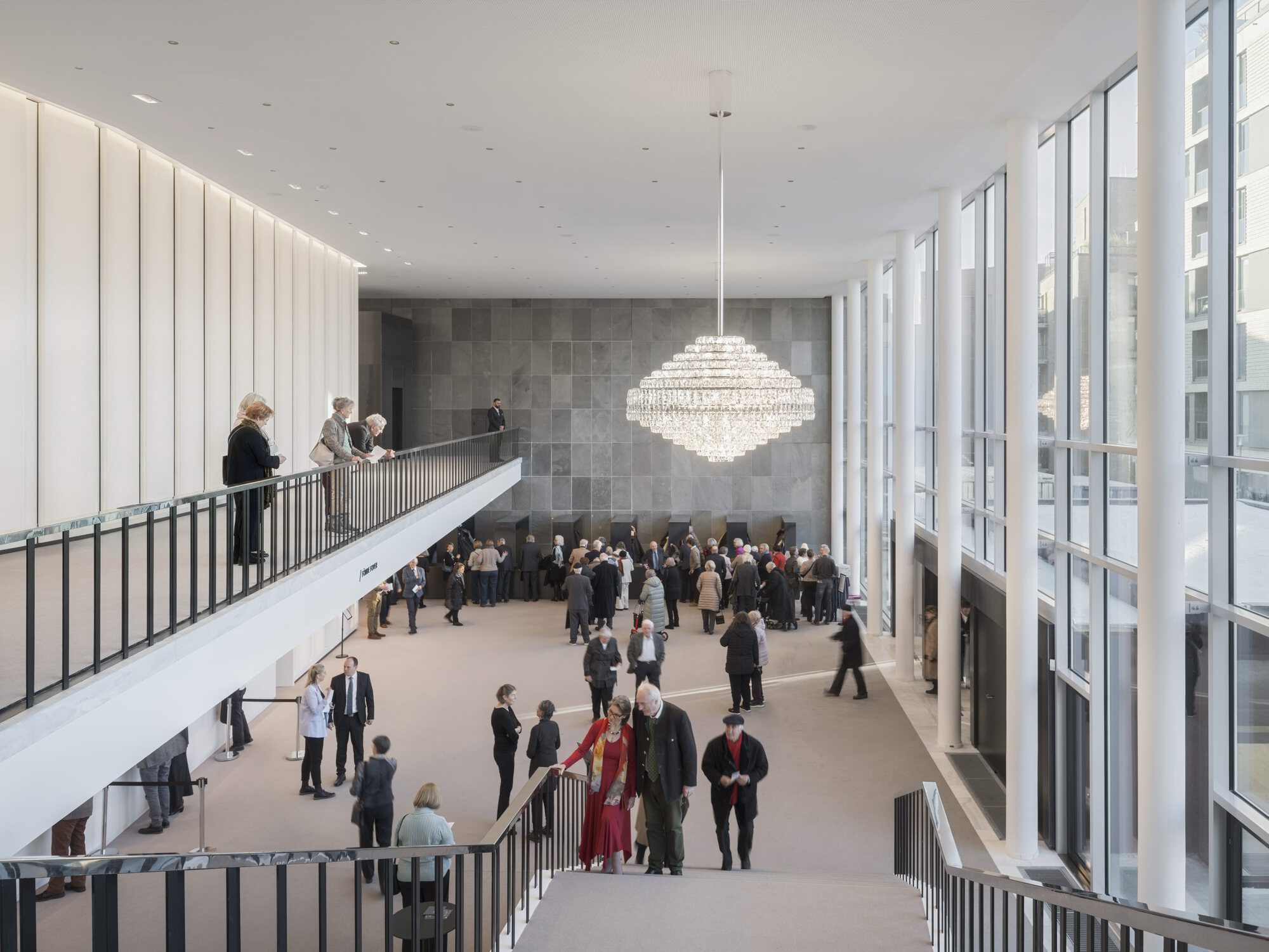 Double-height foyer with staircase and tiered chandelier as concertgoers gather below