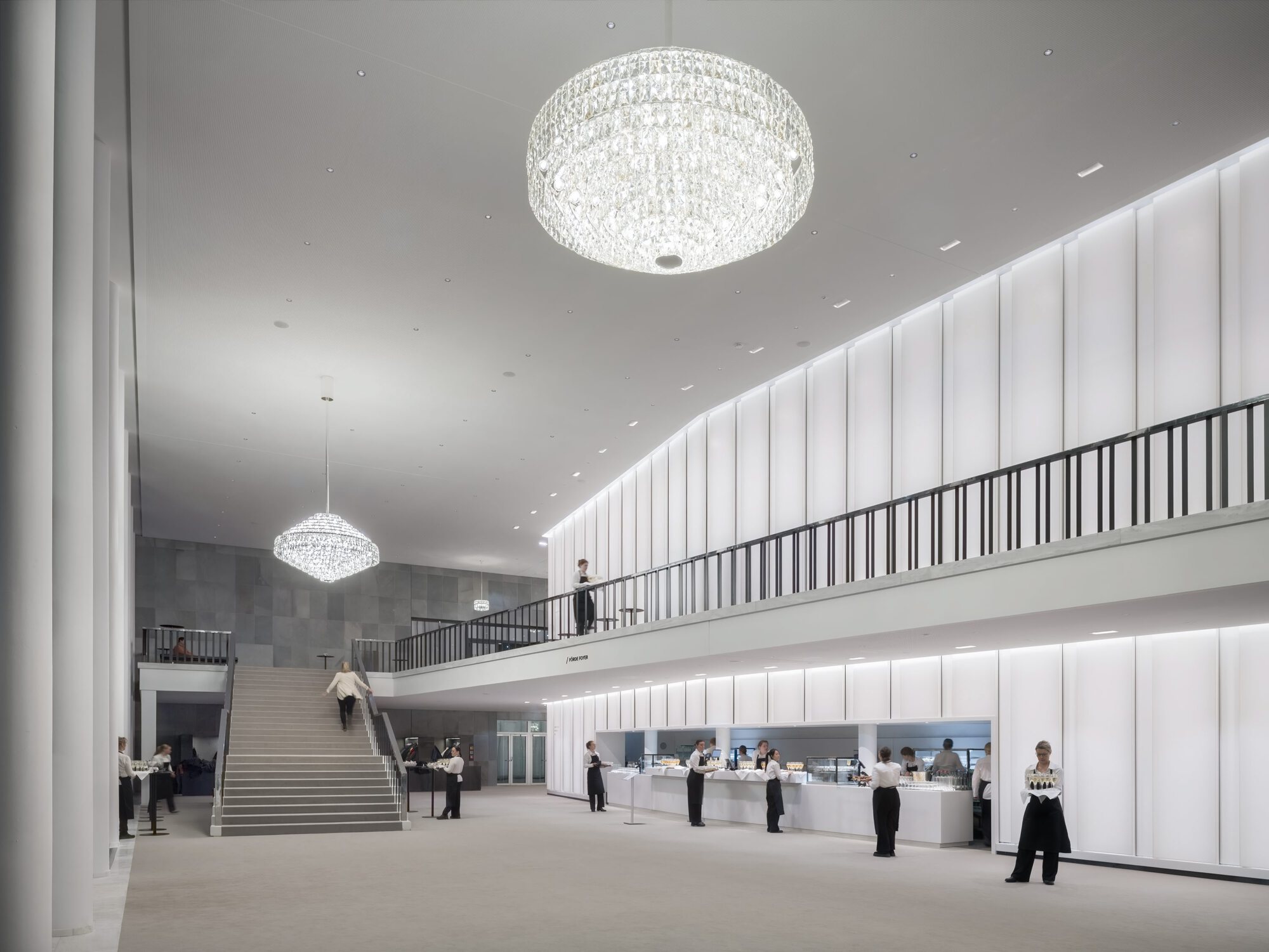 Interior lobby showing wide staircase with white paneled walls and two crystal chandeliers overhead