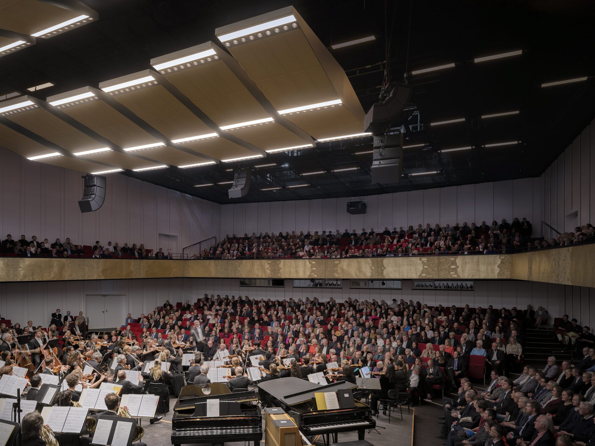 Concert hall auditorium with tiered seating filled with audience members and orchestra on stage