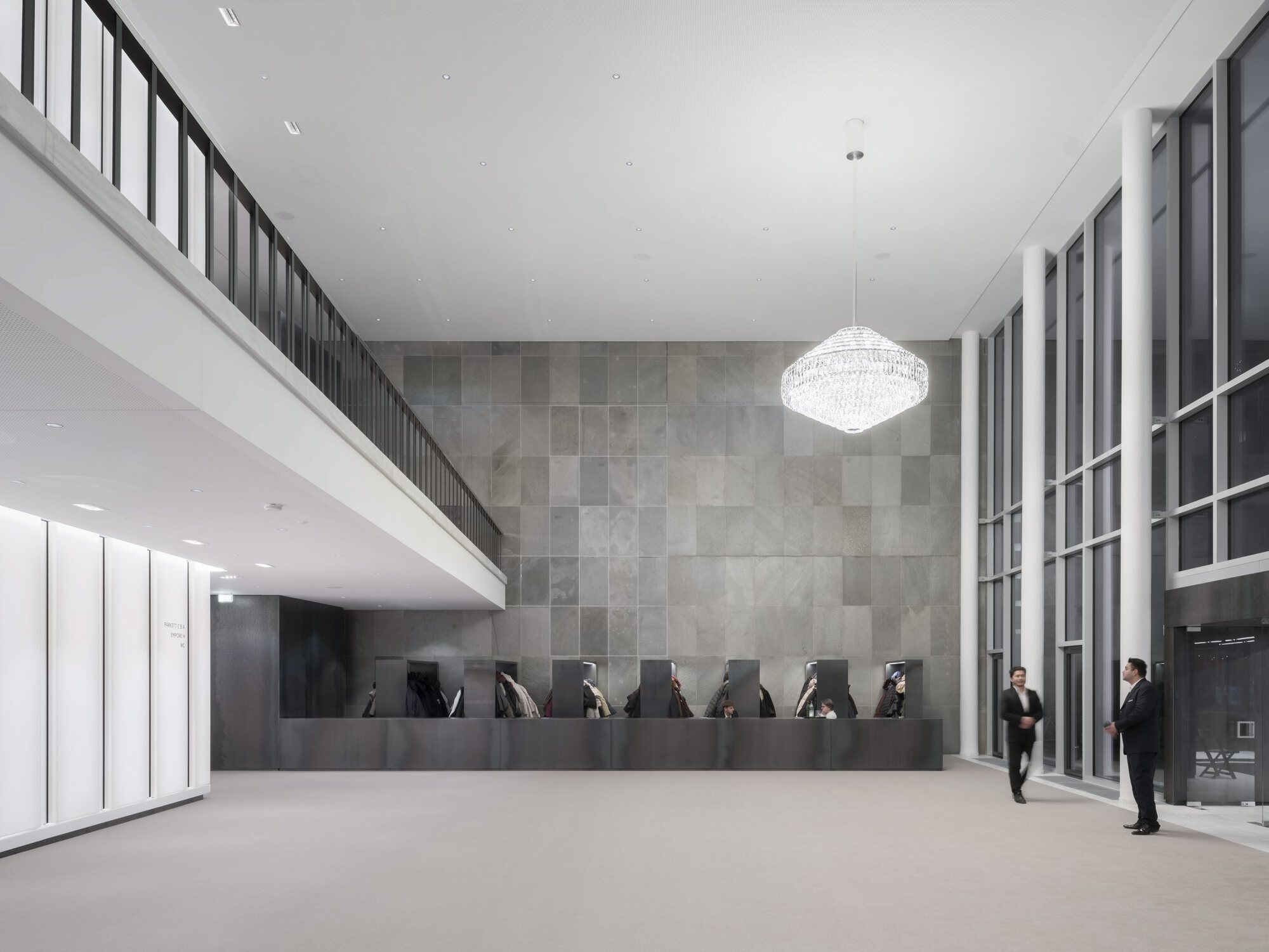 Reception desk with dark stone paneling beneath a mezzanine and crystal chandelier