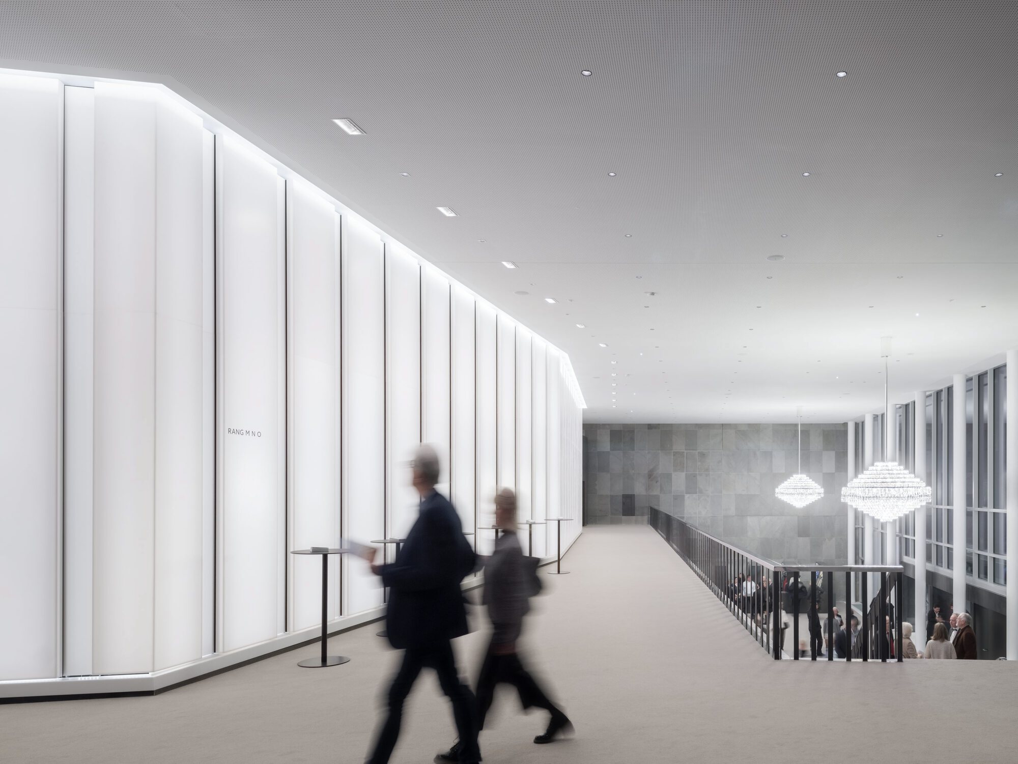 Upper-level corridor with vertical white panels along one wall and two blurred figures walking