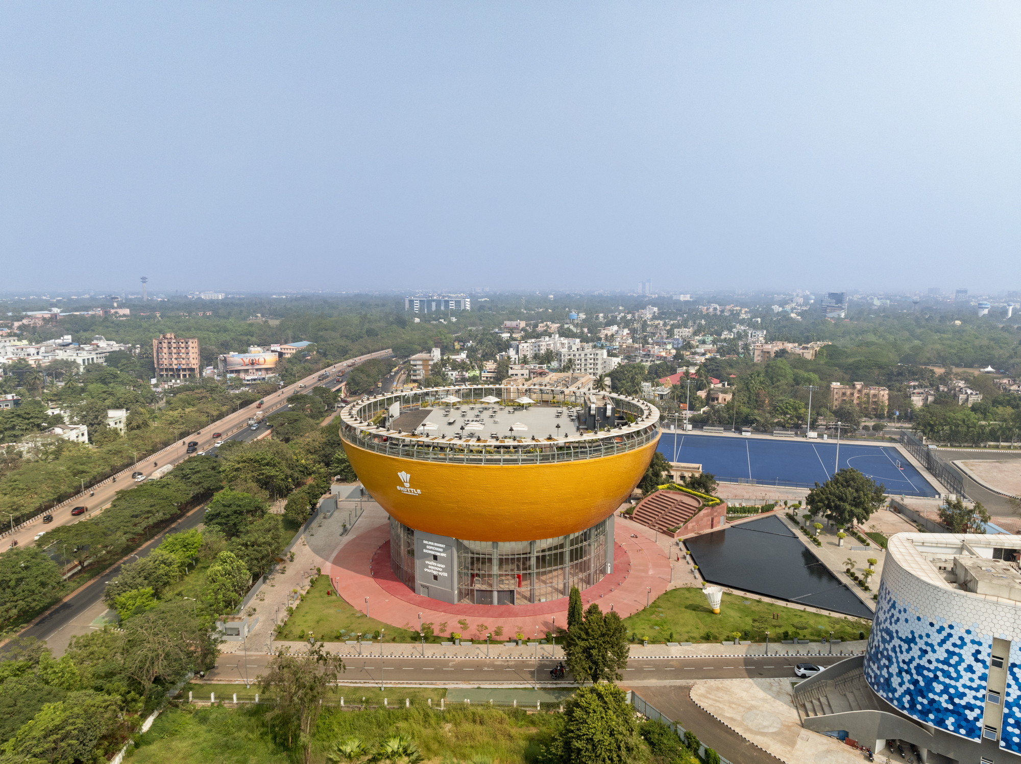 Aerial view of the bowl-shaped yellow volume with rooftop terrace overlooking surrounding roads and residential blocks