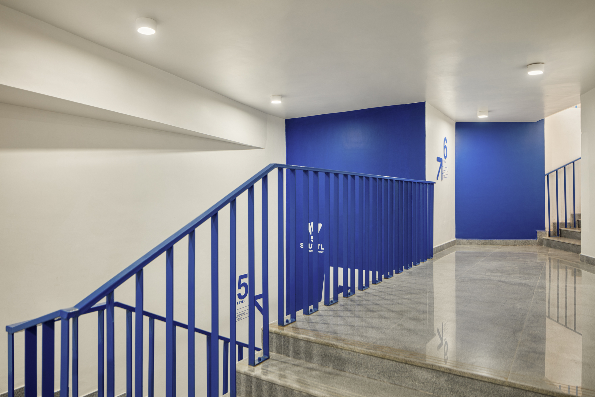 Concrete staircase with blue metal railings and wall panels under recessed ceiling lights