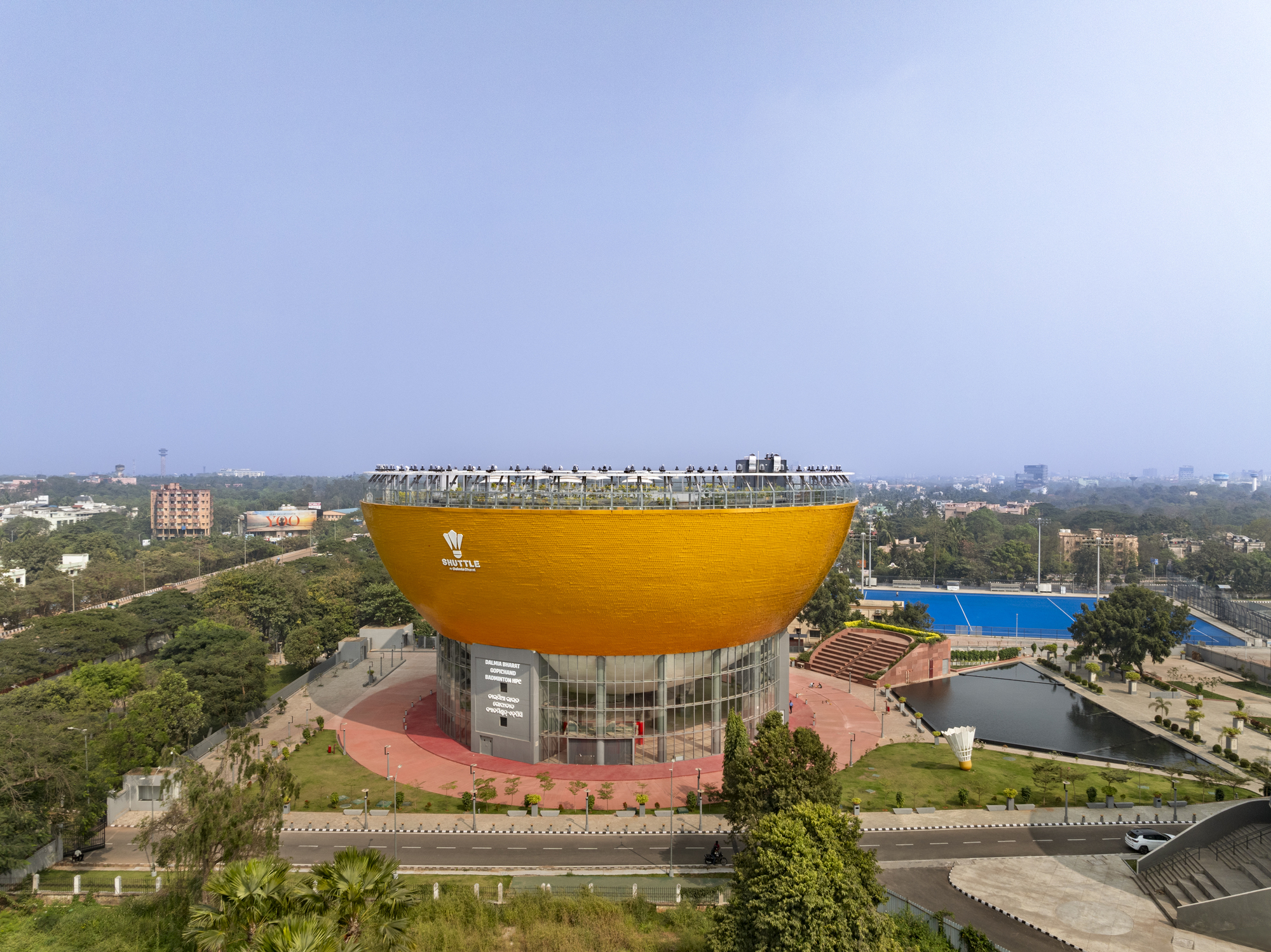 Aerial view of the golden dome-shaped volume rising above a glass base with red paved surroundings