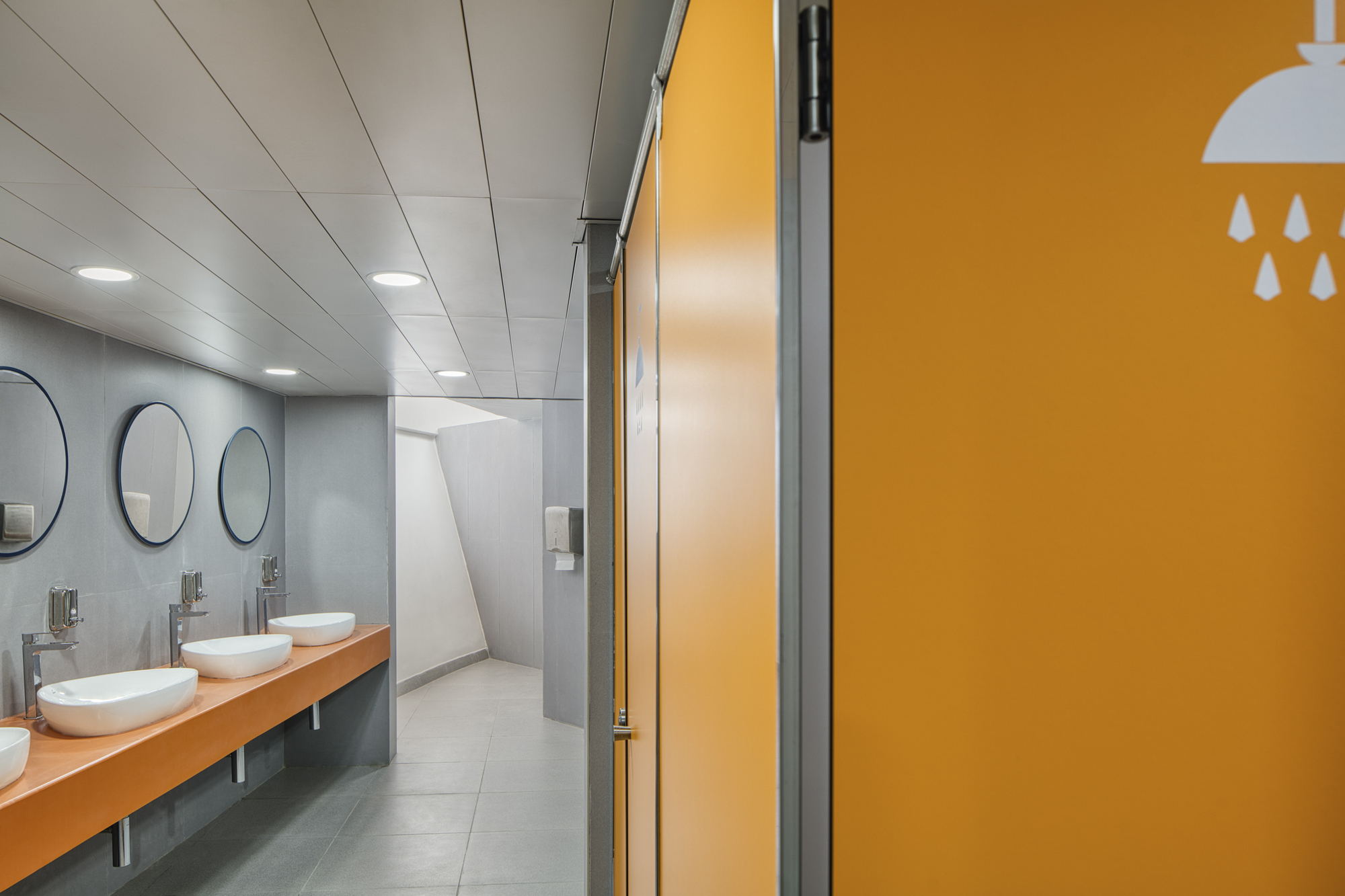 Washroom with three round mirrors above white vessel sinks on a timber counter and yellow partition panels