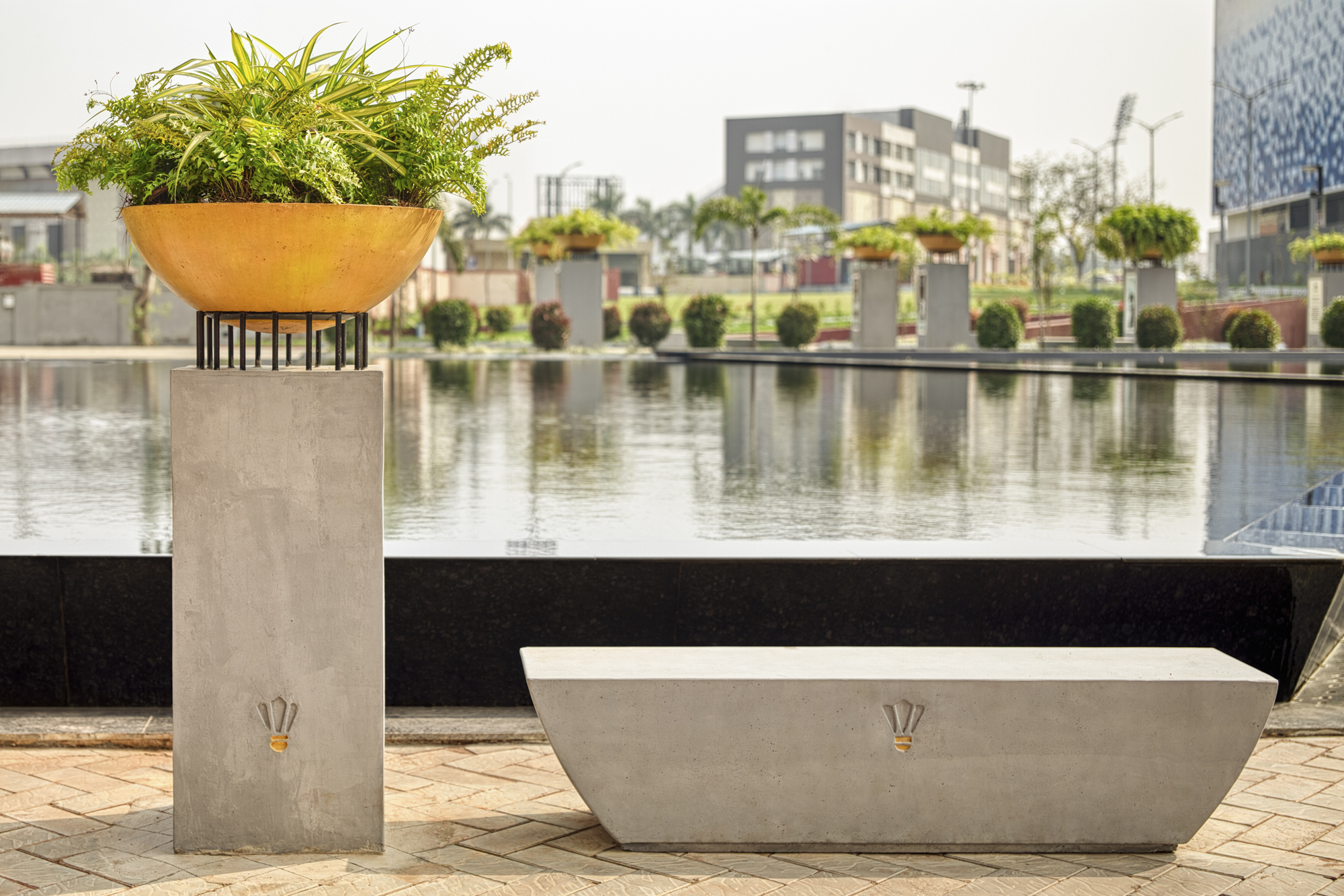 Concrete planter column and seating bench beside a reflecting pool with distant buildings