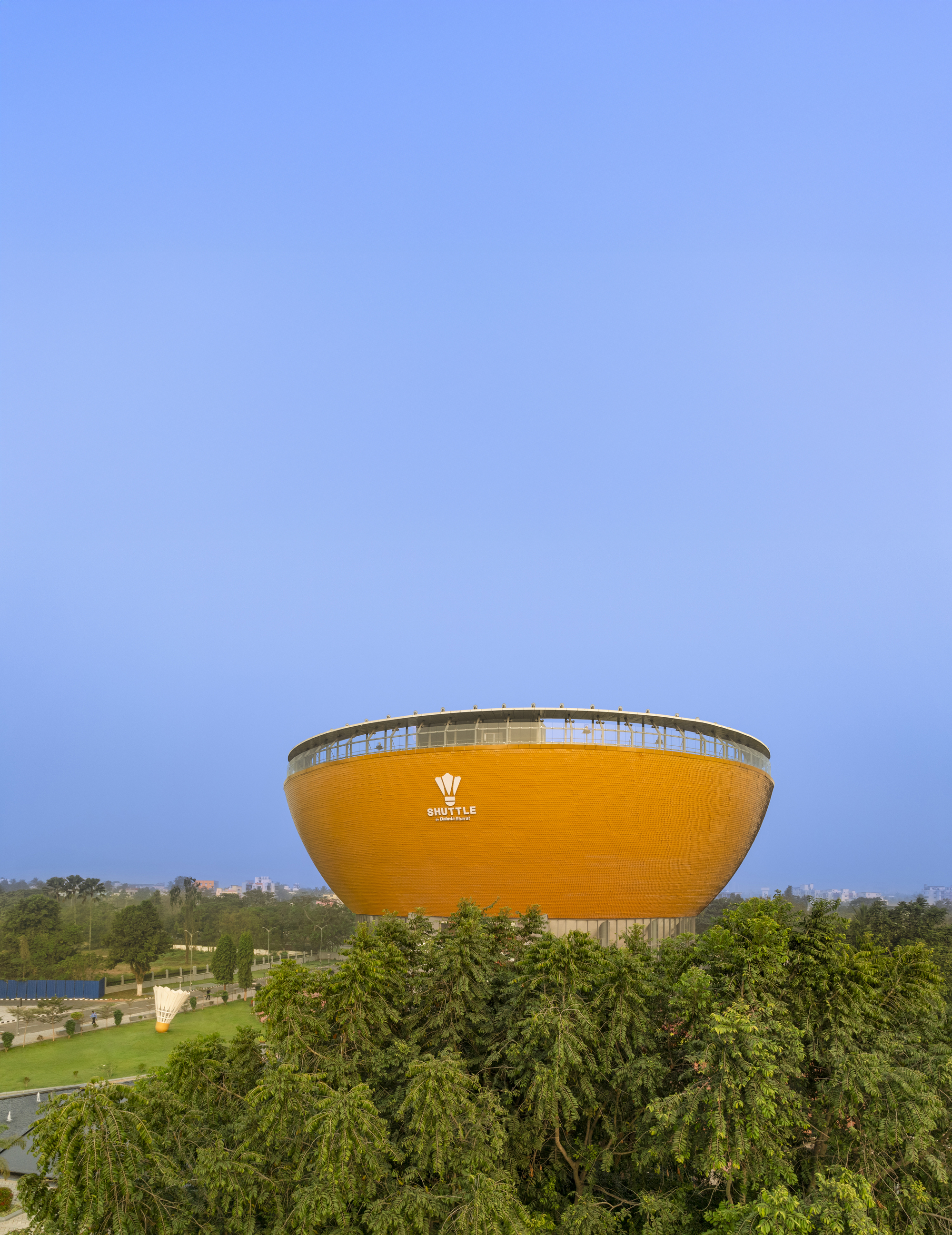 Exterior view of the elevated orange bowl-shaped volume rising above surrounding trees at dusk