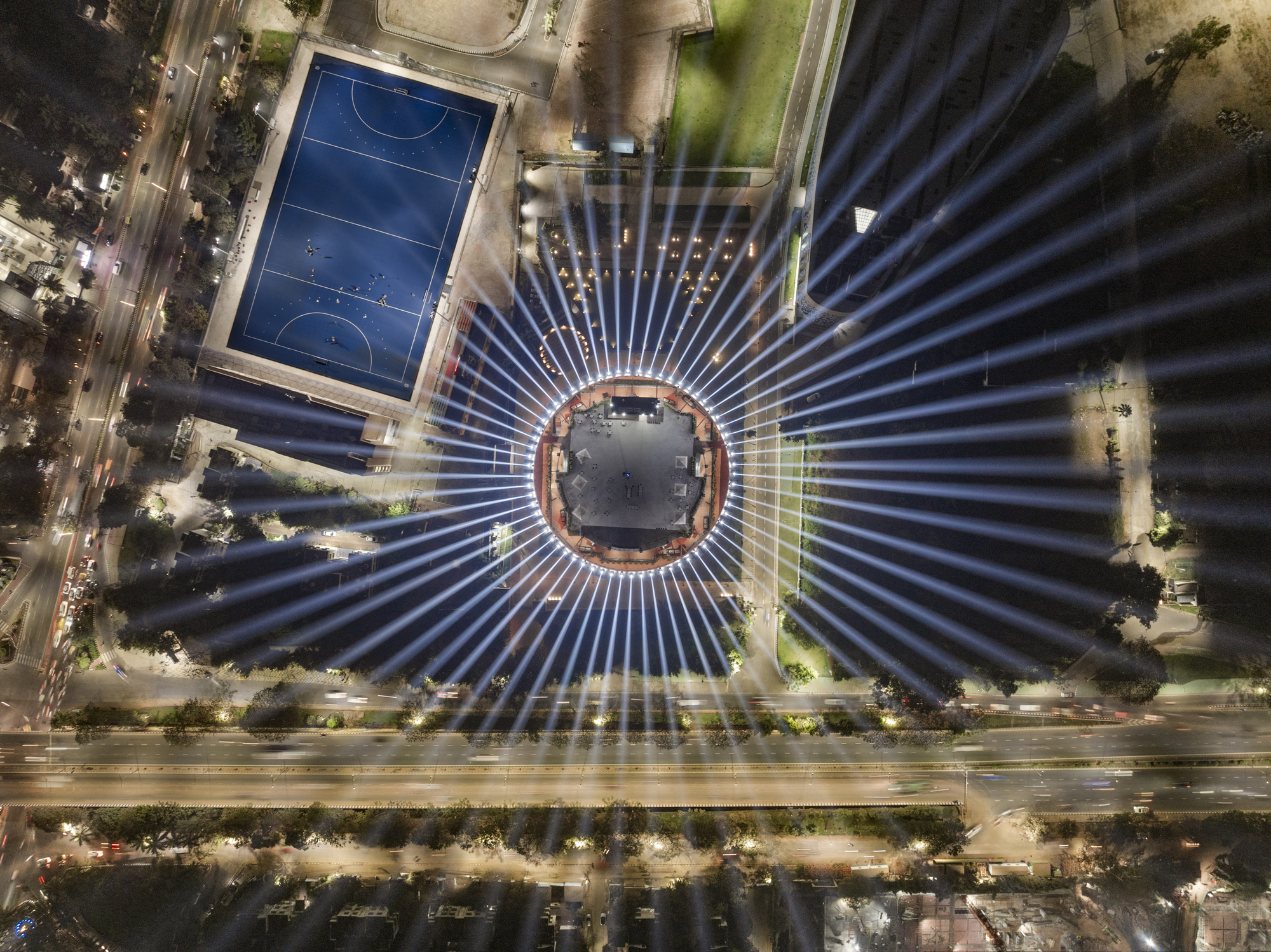 Aerial view at night showing radial light beams emanating from the circular structure