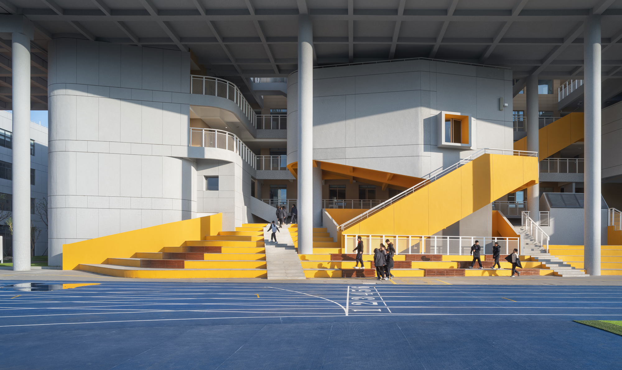 Covered courtyard with bright yellow staircase and amphitheater steps beneath a coffered ceiling supported by white columns