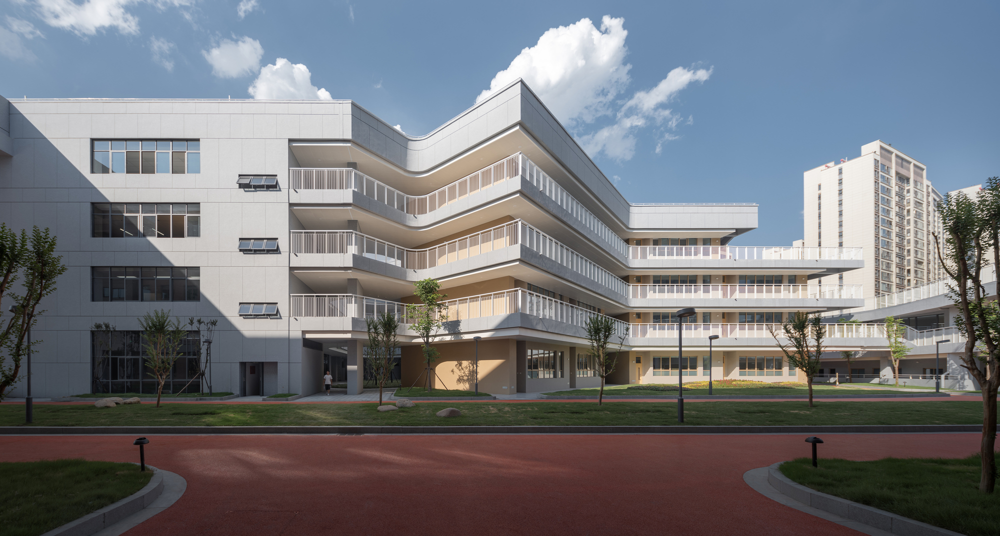 Stacked horizontal facade with continuous ribbon windows overlooking a landscaped lawn and running track