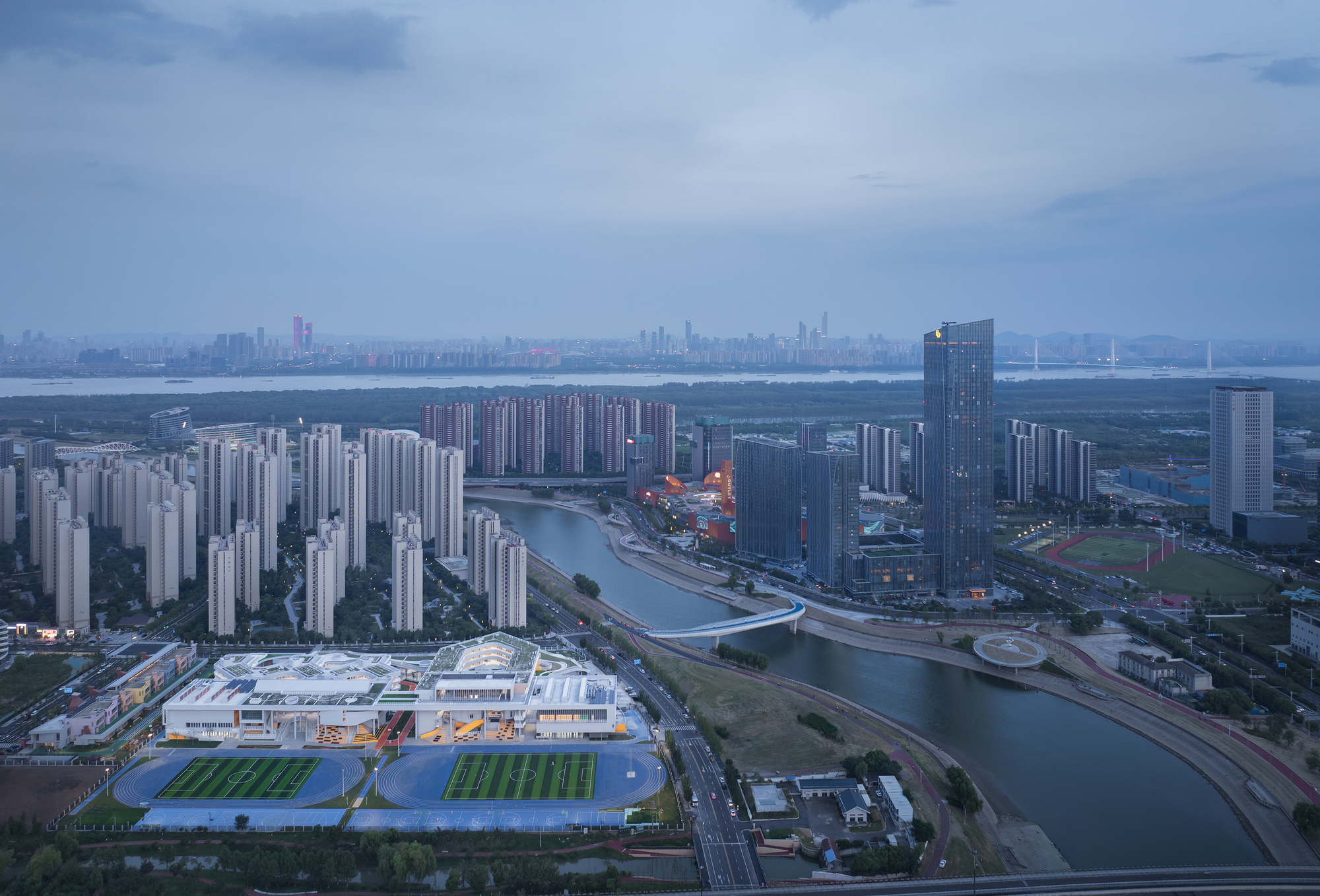 Aerial view of the white rooftop with two green sports fields beside a winding canal at dusk