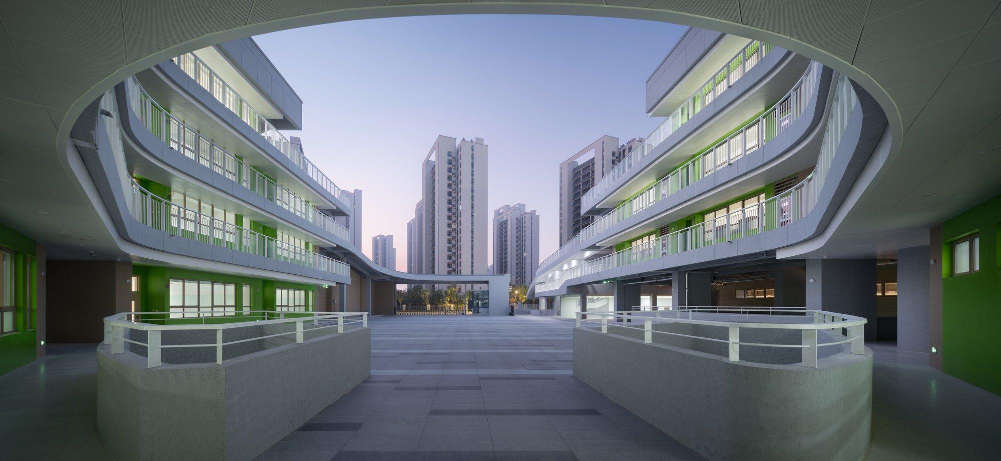 View through an elliptical courtyard opening toward high-rise towers at dusk