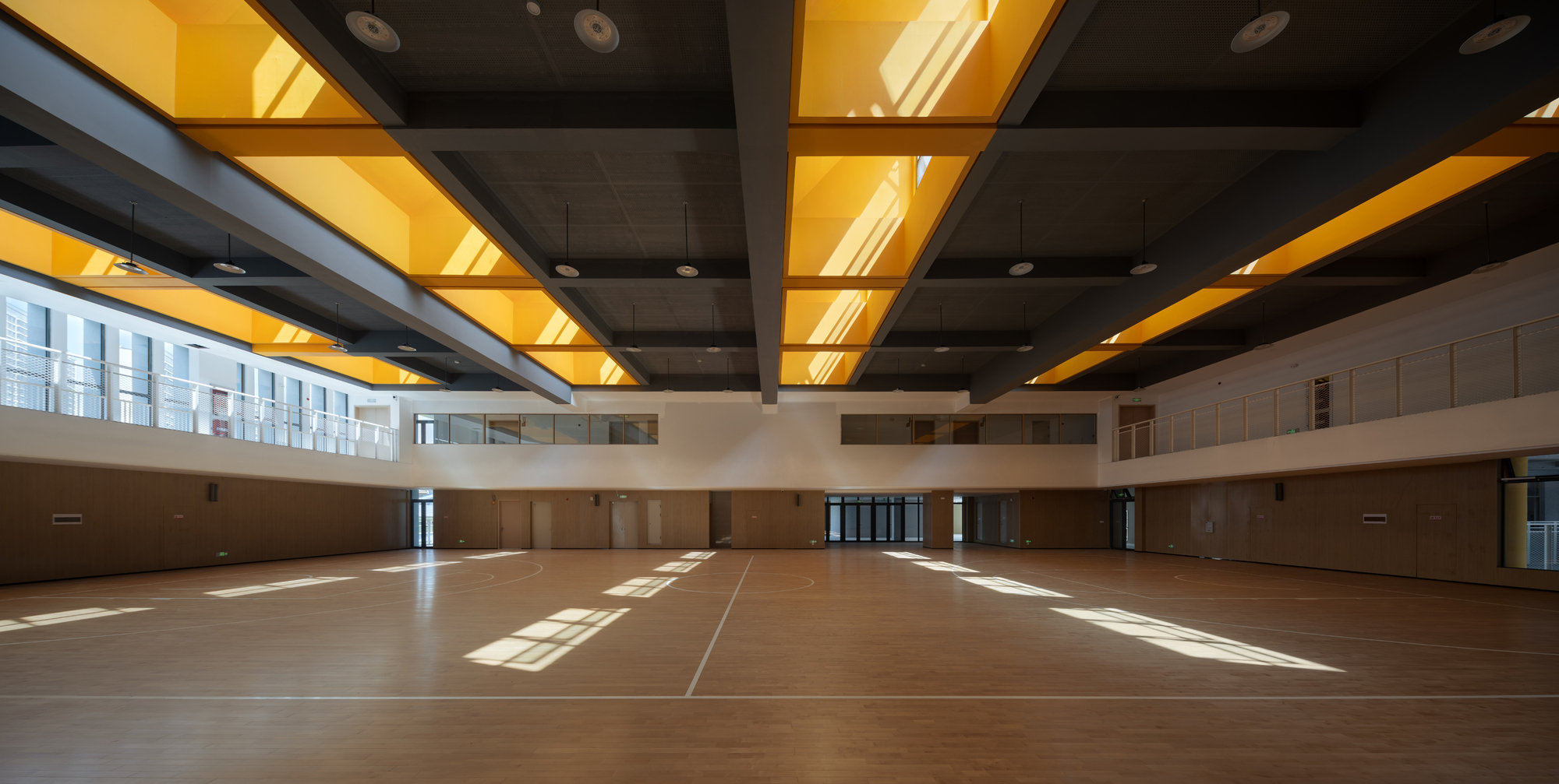 Gymnasium floor with timber surface beneath alternating grey and yellow coffered ceiling panels in sunlight