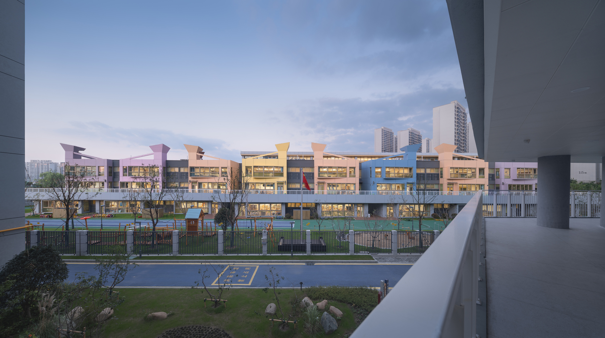 View across landscaped courtyard toward illuminated facades and colorful canopy elements at dusk