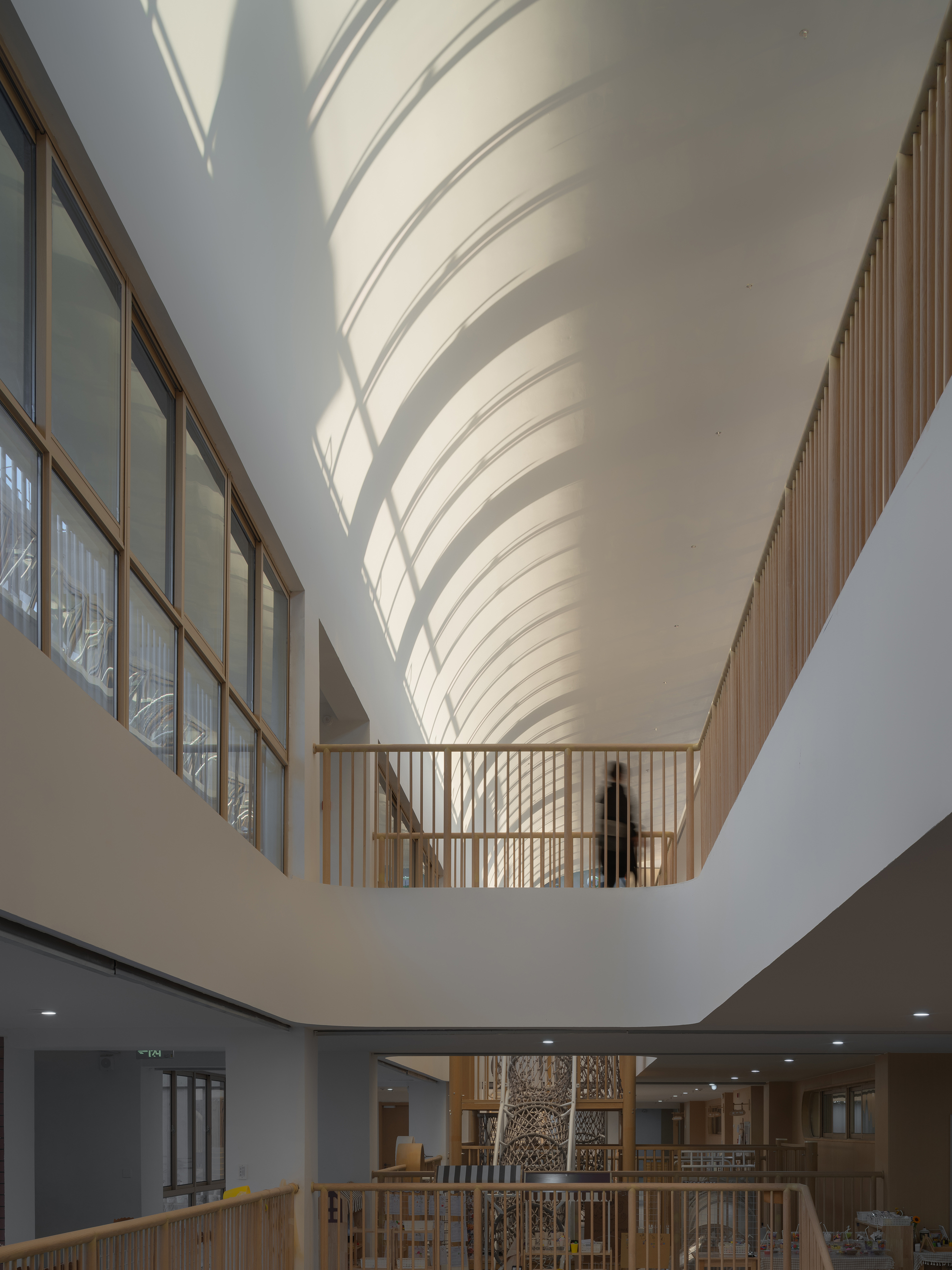 Interior atrium with sculptural ribbed ceiling, timber balustrades, and glazed corridor overlooking the central void