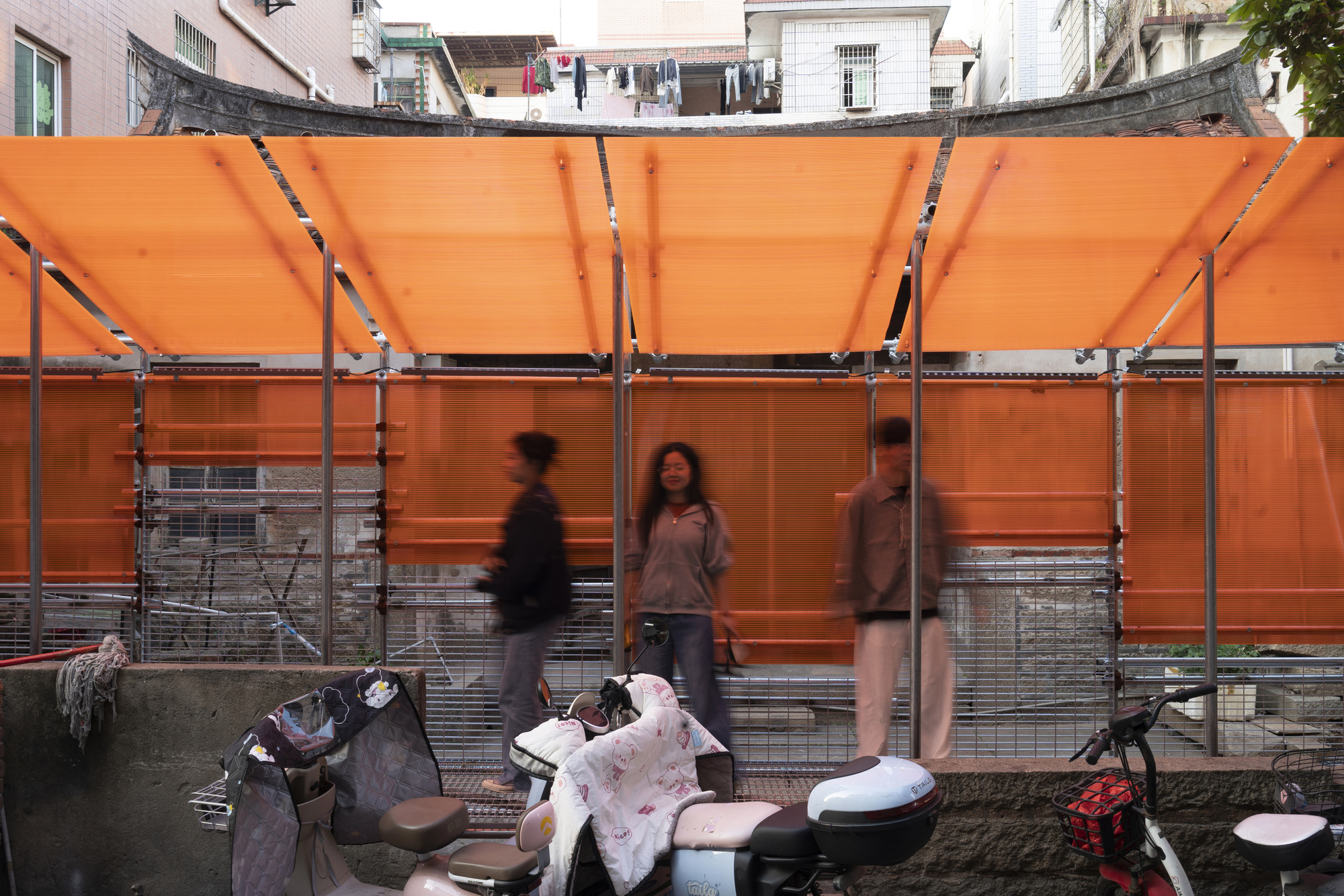 Translucent orange panels and steel frame with pedestrians gathering on scooters below