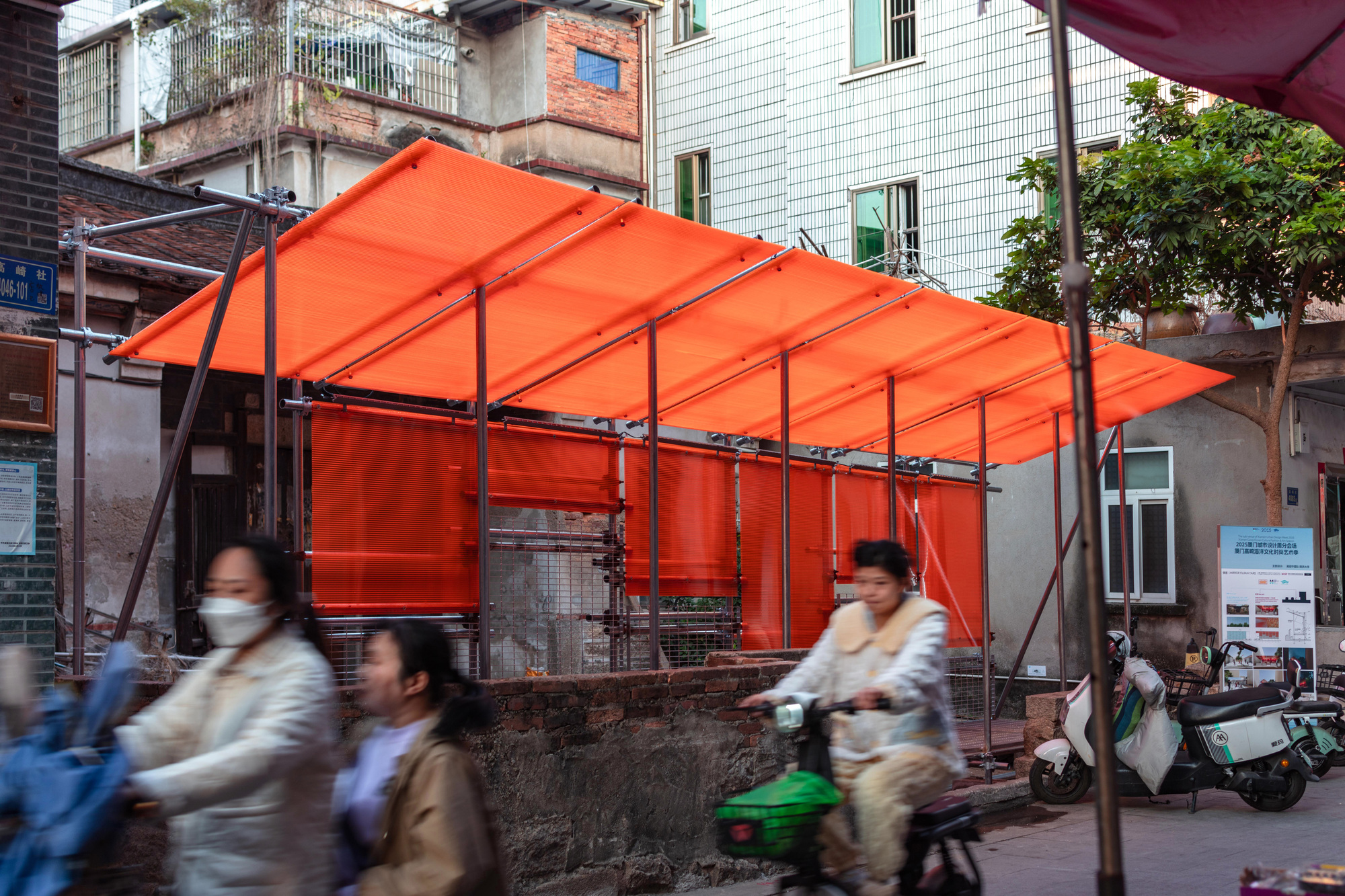 Orange fabric canopy with steel frame above a street corner as pedestrians pass by in motion blur