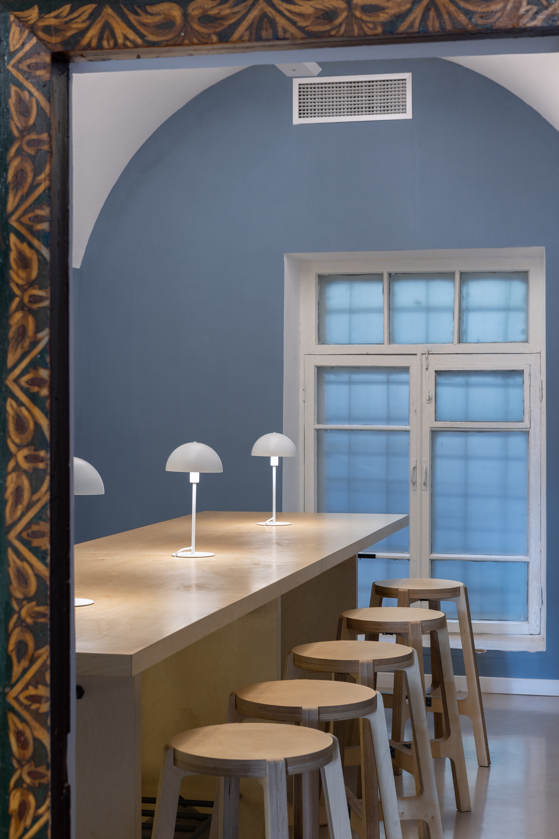 View through ornate doorframe to blue arched dining area with timber counter and mushroom lamps